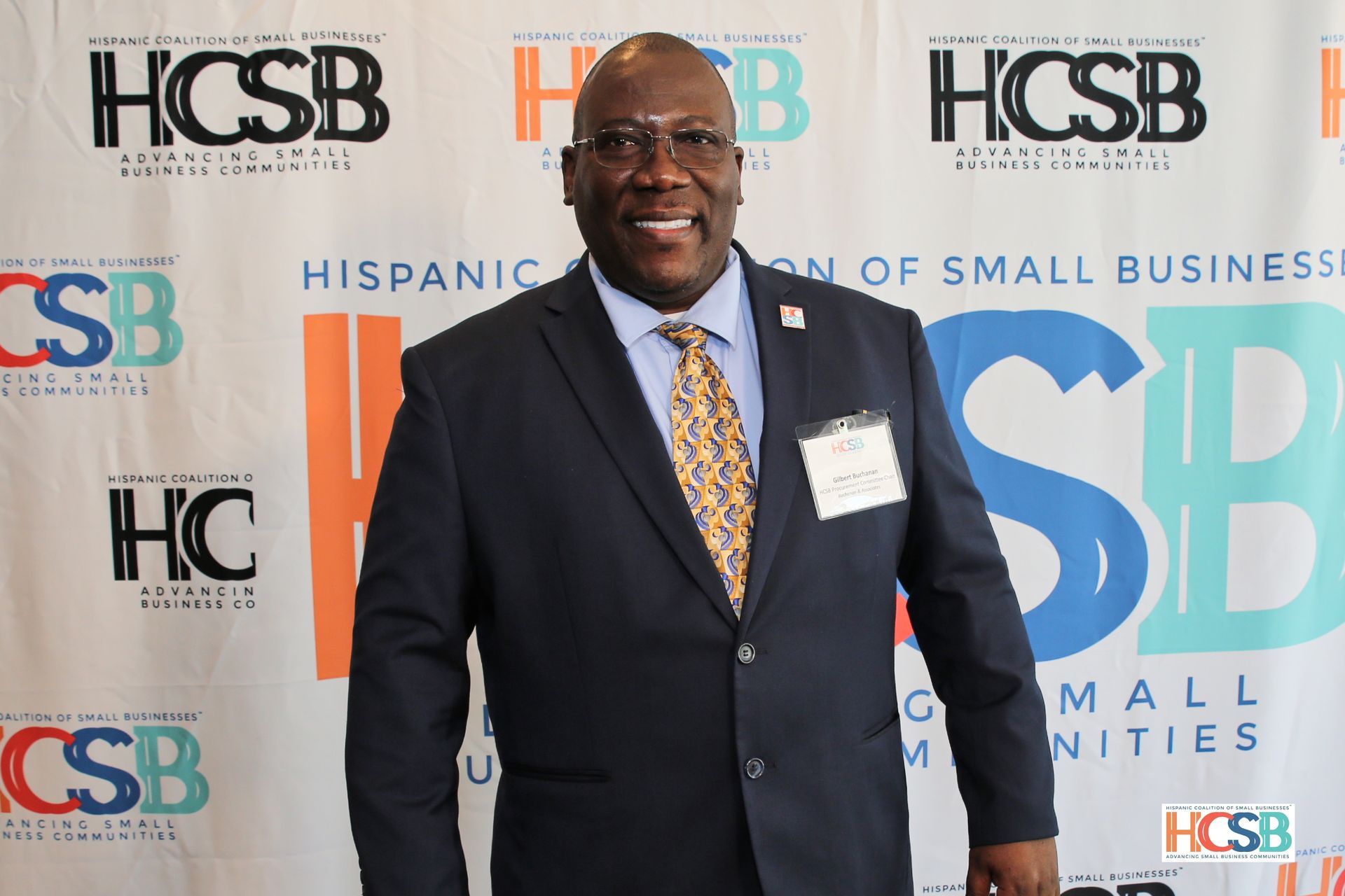 A man in a suit and tie is standing in front of a hcsb banner