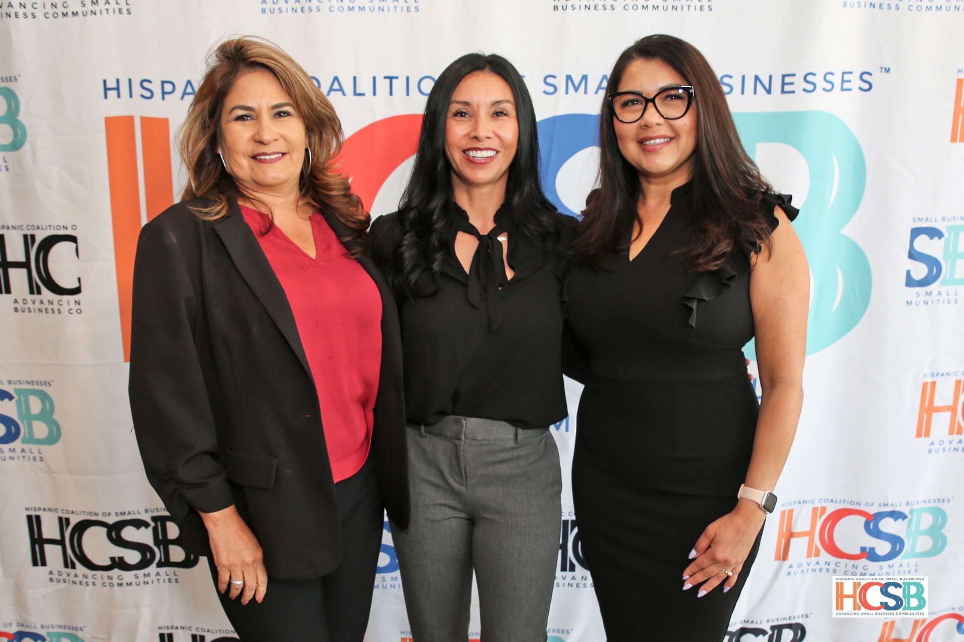 Three women are posing for a picture in front of a hcsb banner.