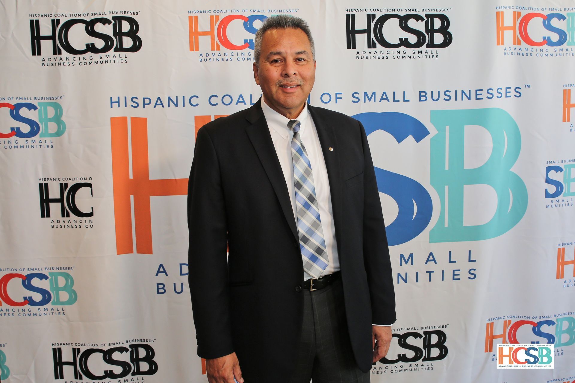 A man in a suit and tie is standing in front of a hcsb banner