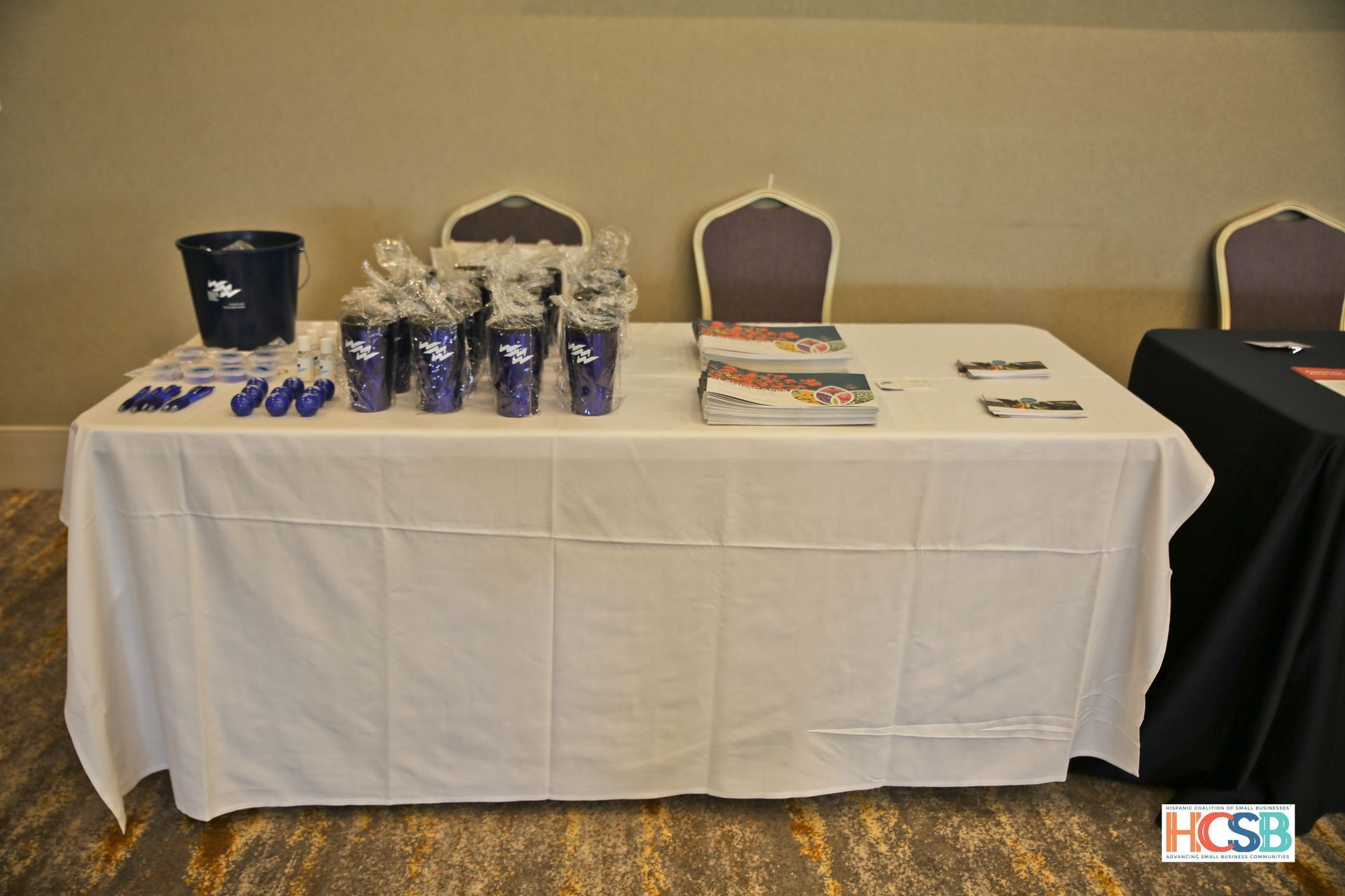 A table with a white table cloth and a bucket of popcorn on it.