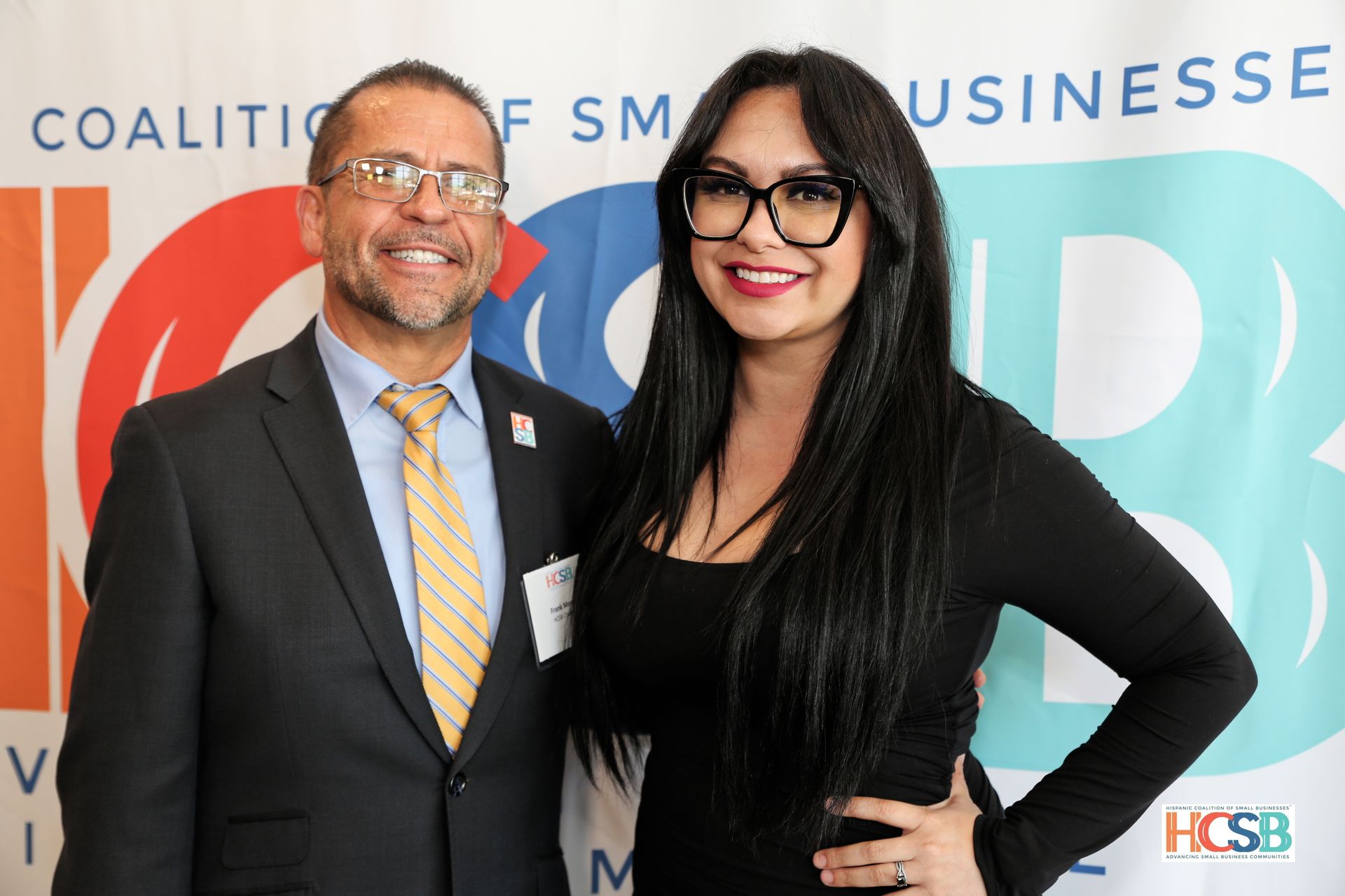 A man and a woman are posing for a picture in front of a coalition of small businesses banner.