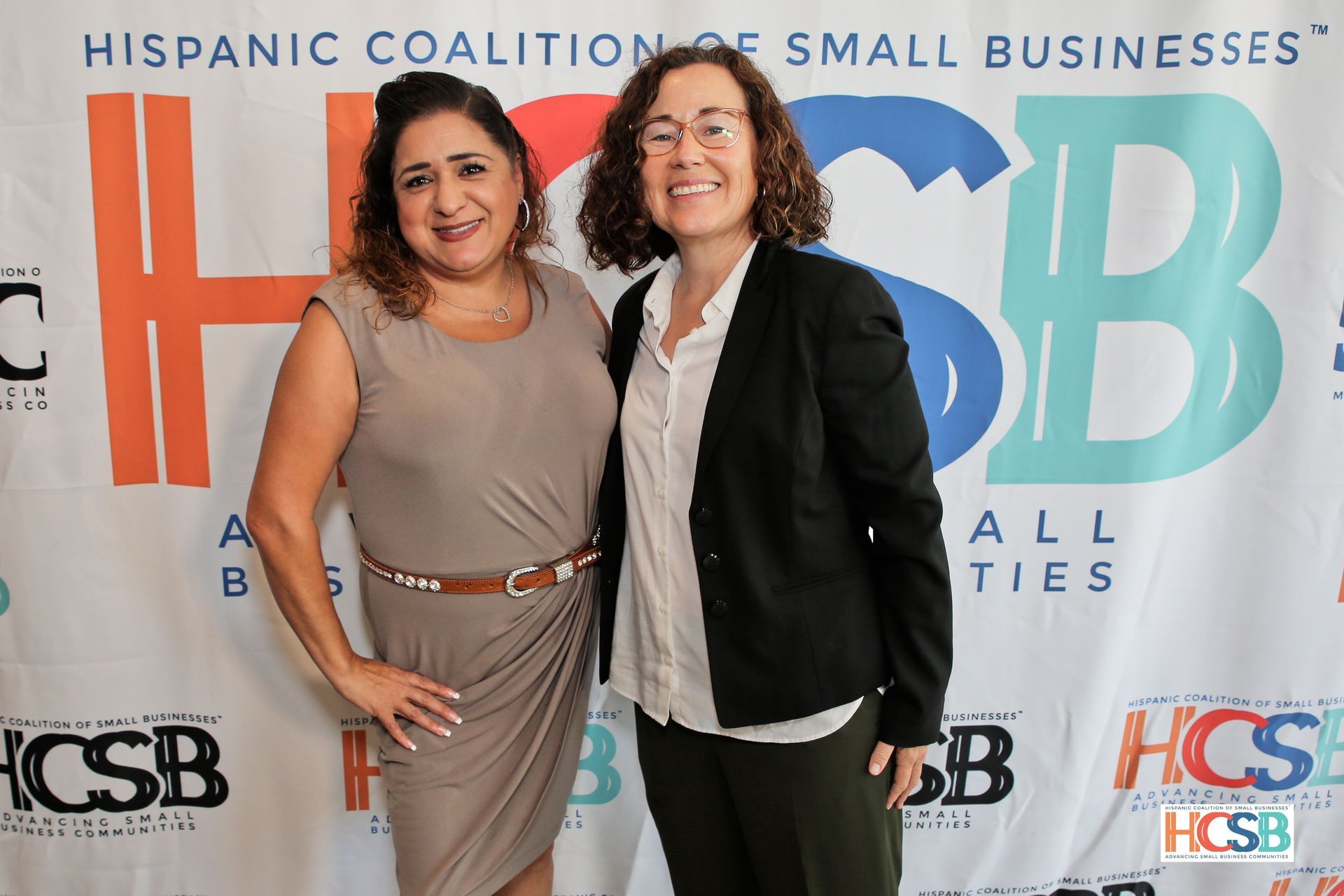 Two women standing in front of a hispanic coalition of small businesses banner