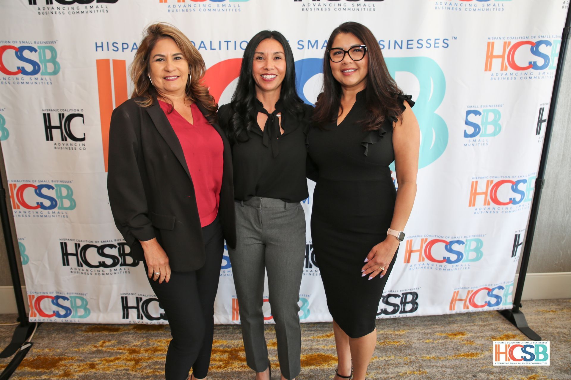 Three women are posing for a picture in front of a backdrop.