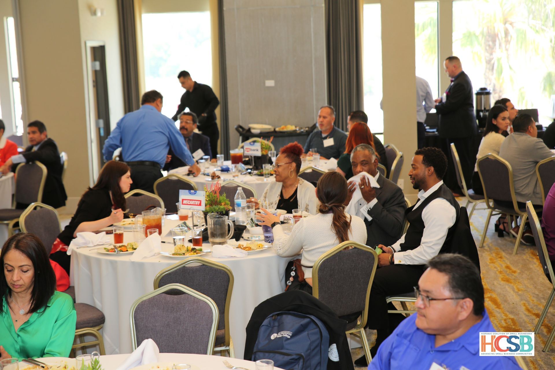 A group of people are sitting at tables in a room with a fcsb logo in the corner
