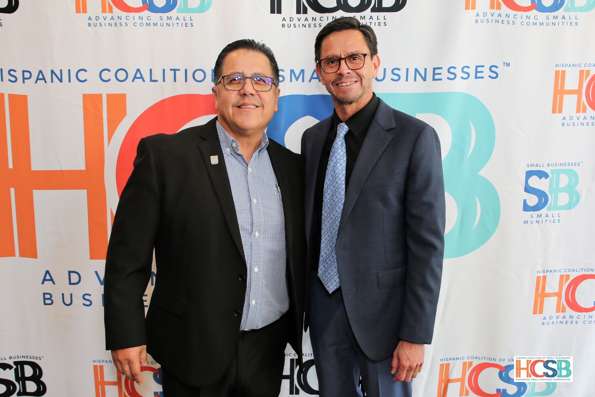 Two men are posing for a picture in front of a sign that says hispanic coalition