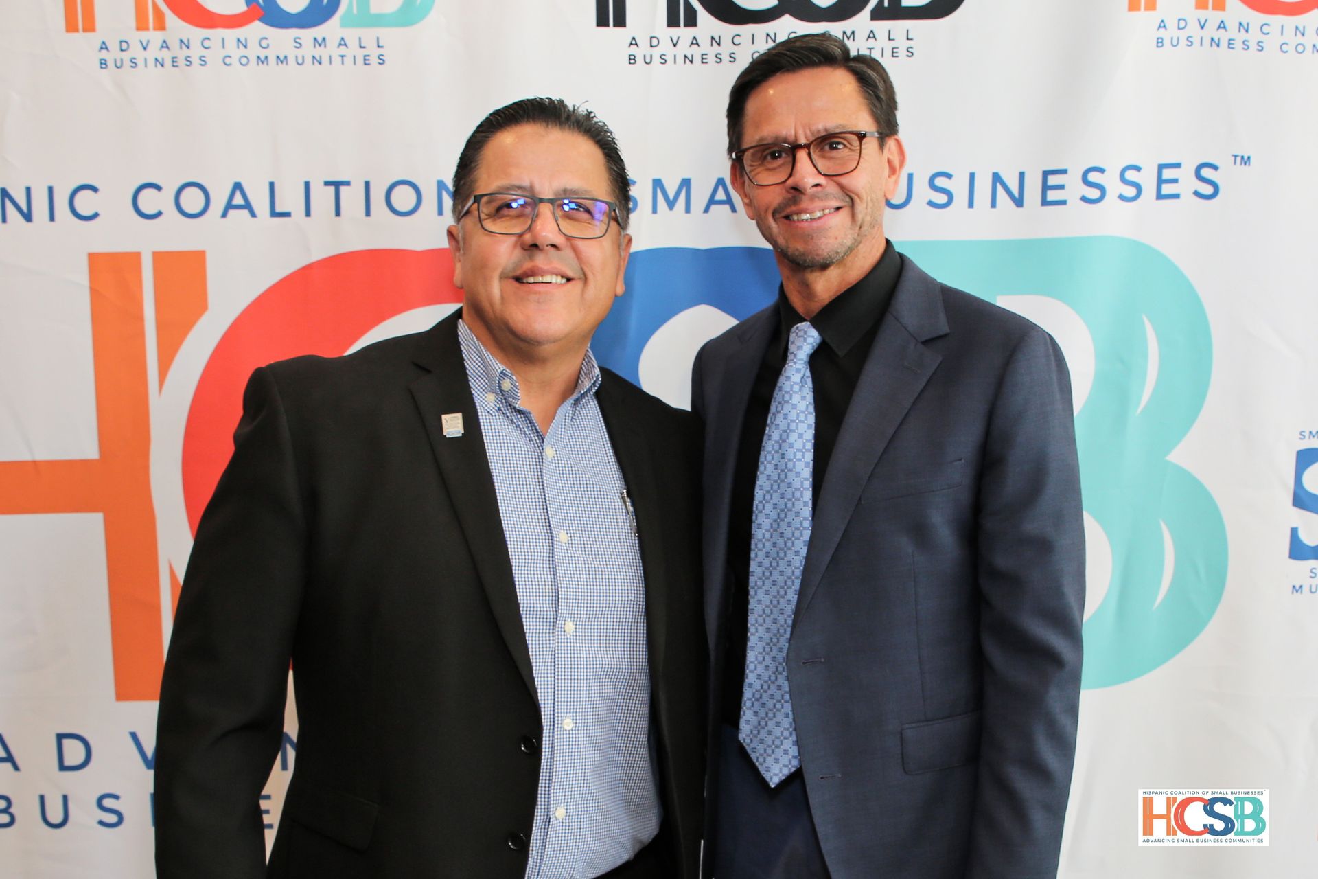 Two men are posing for a picture in front of a hcsb banner