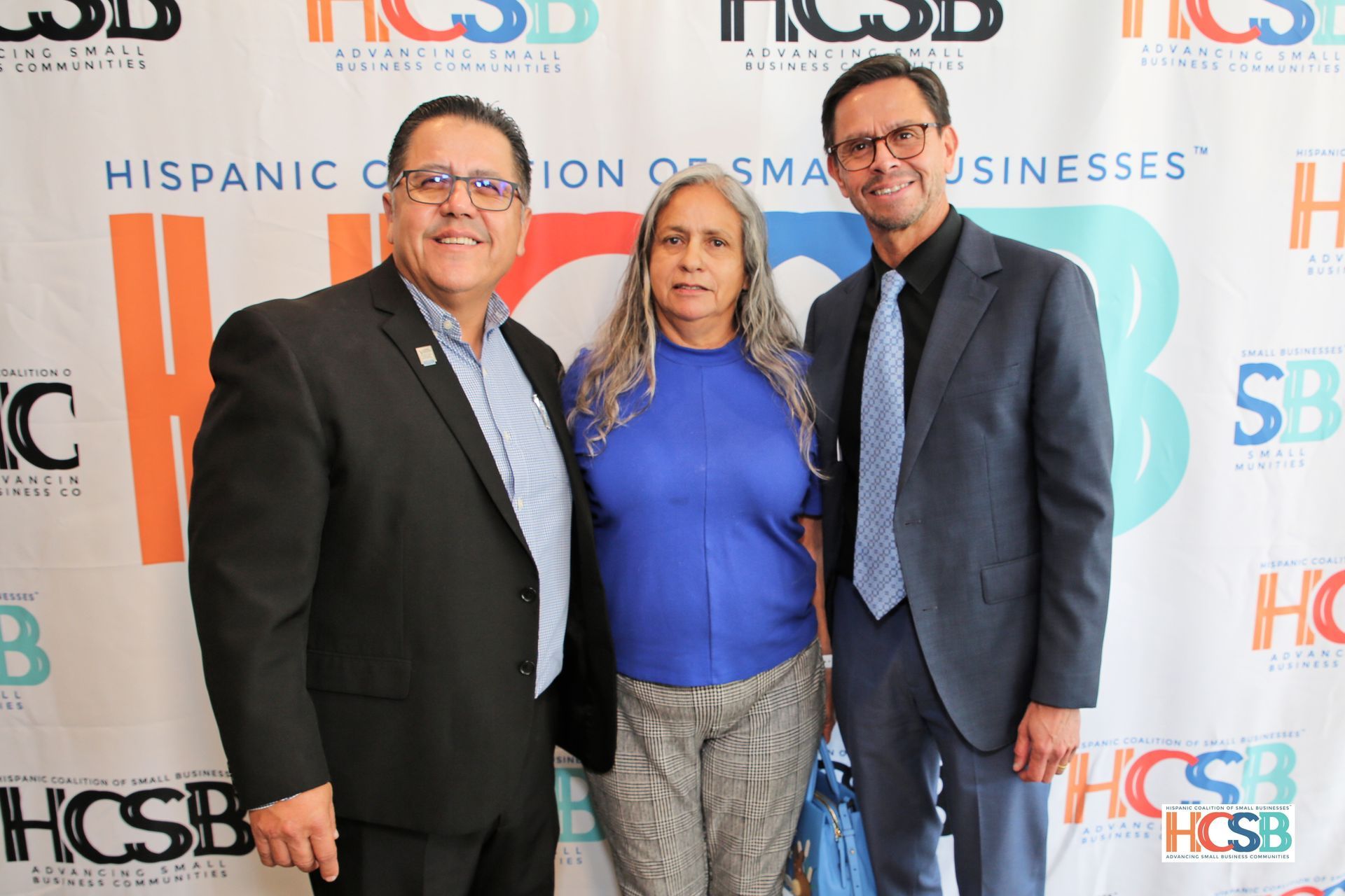 Three people are posing for a picture in front of a banner that says hispanic creation of small businesses.