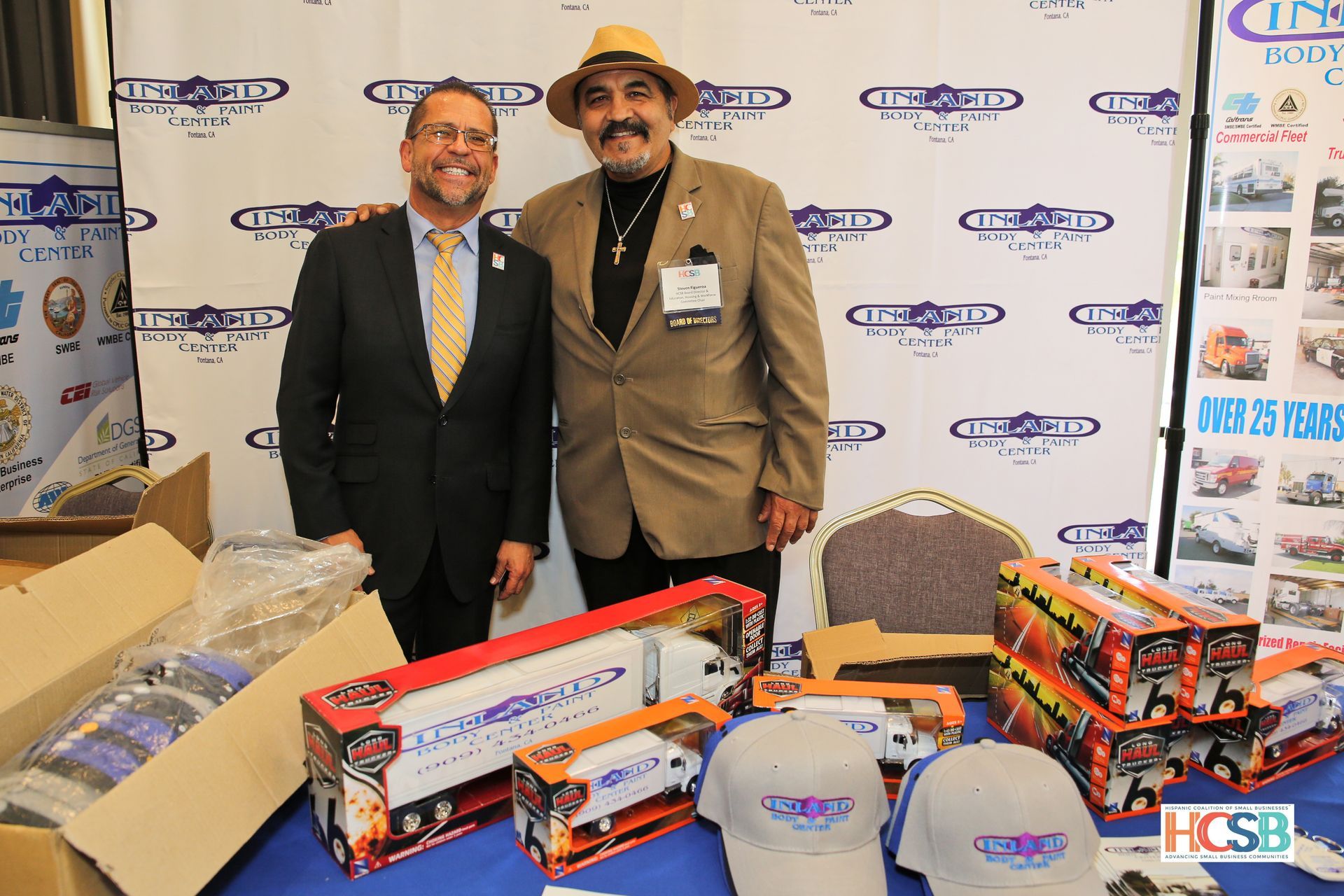 Two men standing next to each other in front of a table full of toy cars