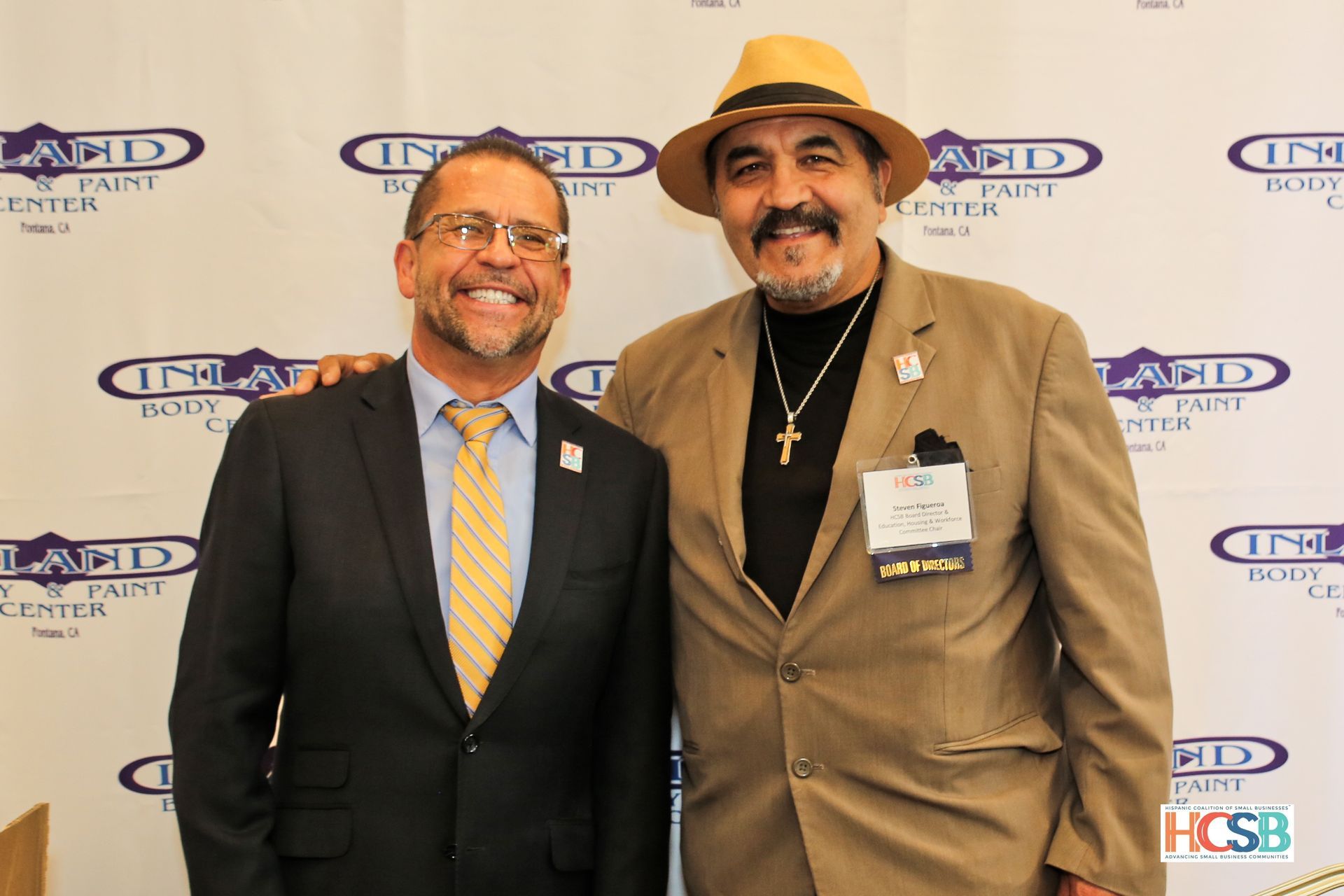 Two men are posing for a picture in front of a wall that says land