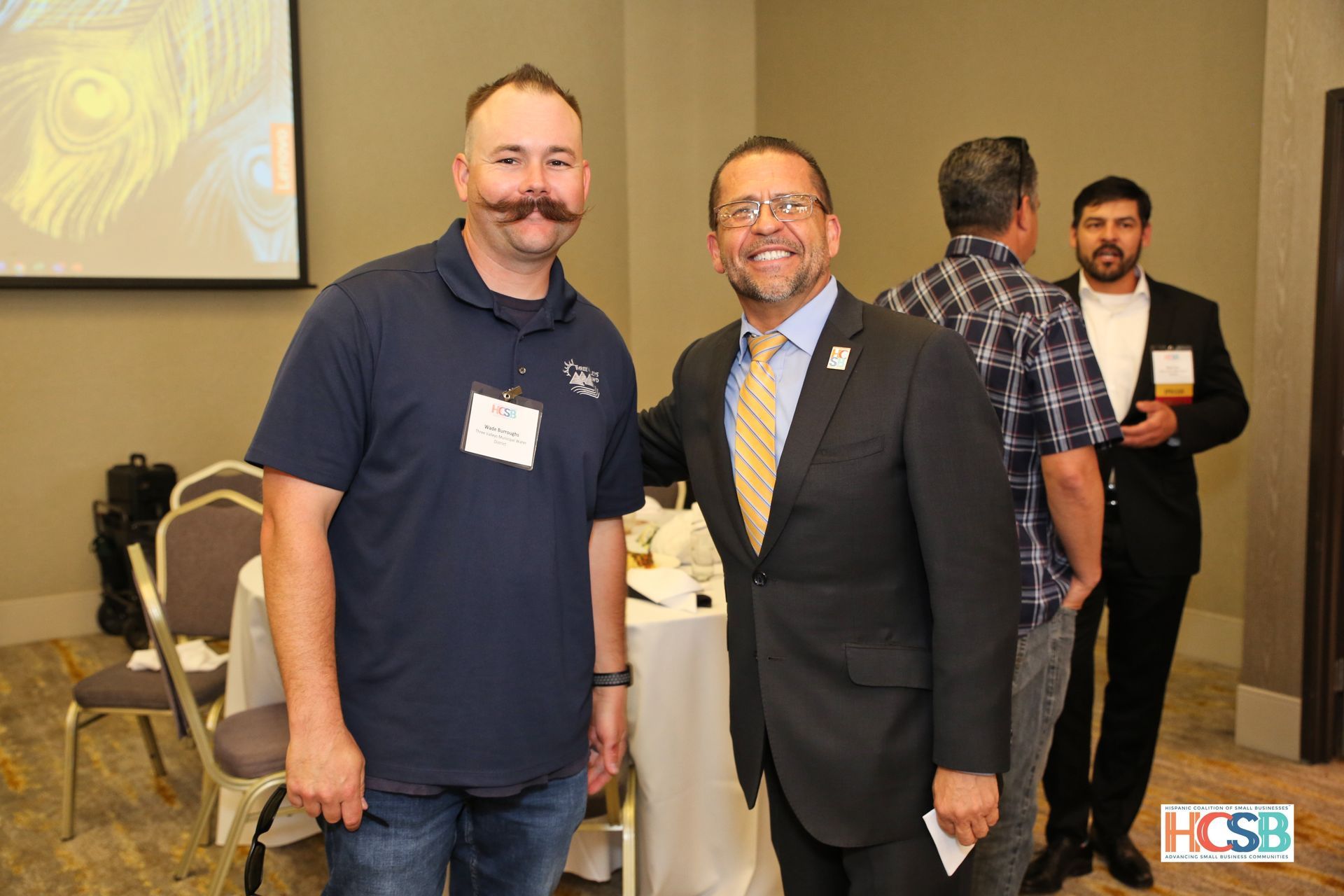 Two men with mustaches are posing for a picture in a room.