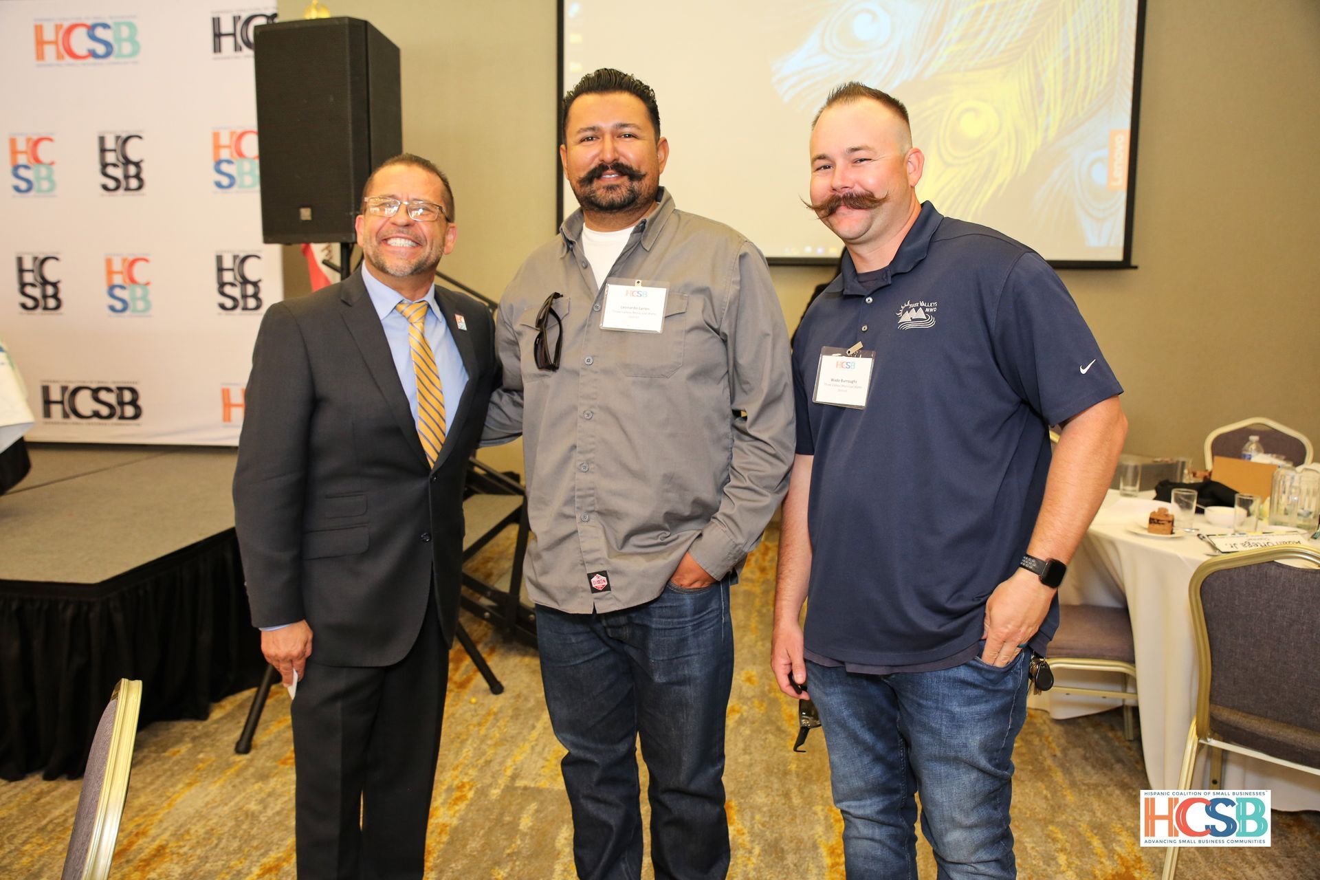 Three men are posing for a picture in front of a projector screen.
