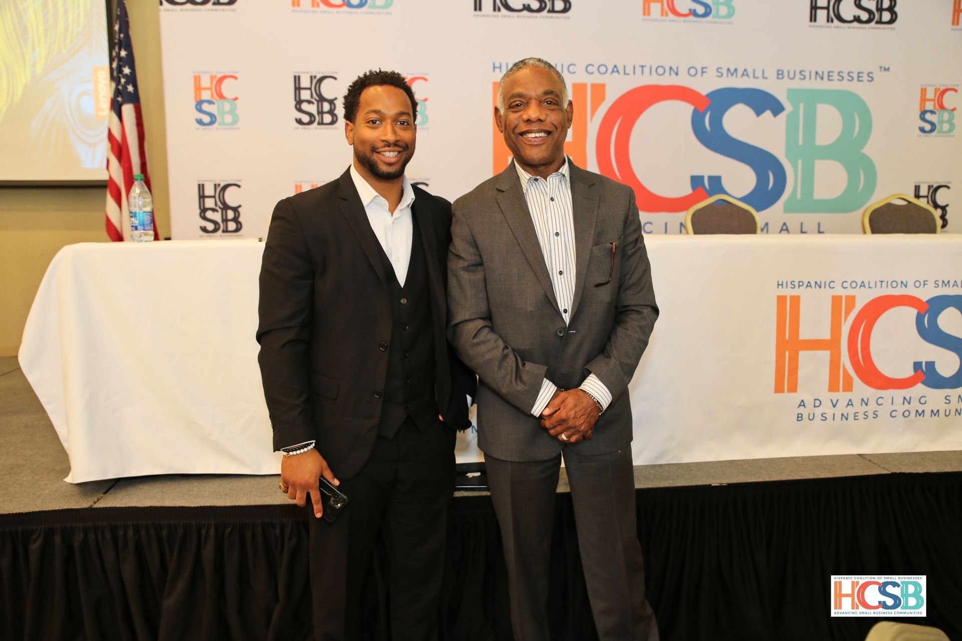 Two men in suits are posing for a picture in front of a hcsb banner.