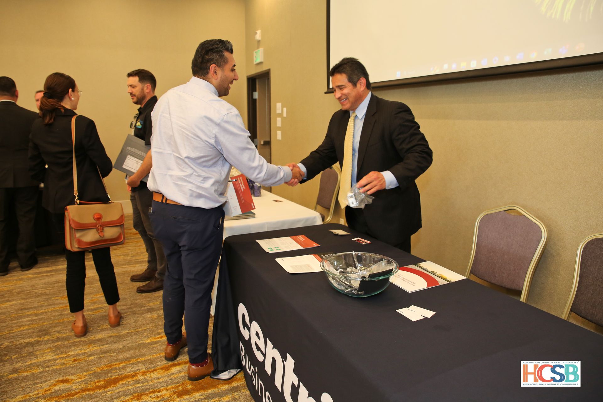 A man in a suit shakes hands with another man at a table.