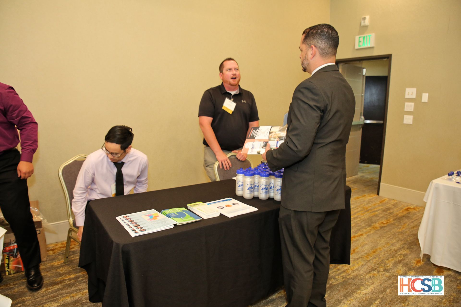 A group of men are standing around a table talking to each other.