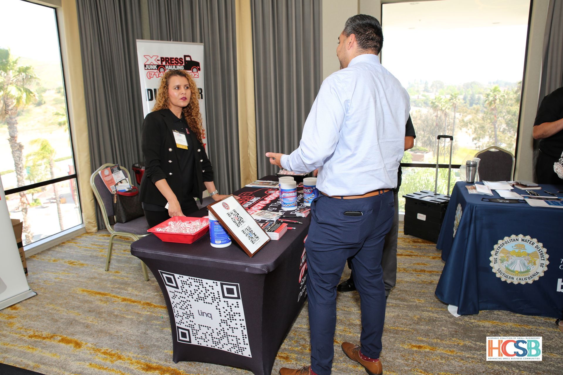 A man and a woman are standing at a table talking to each other.