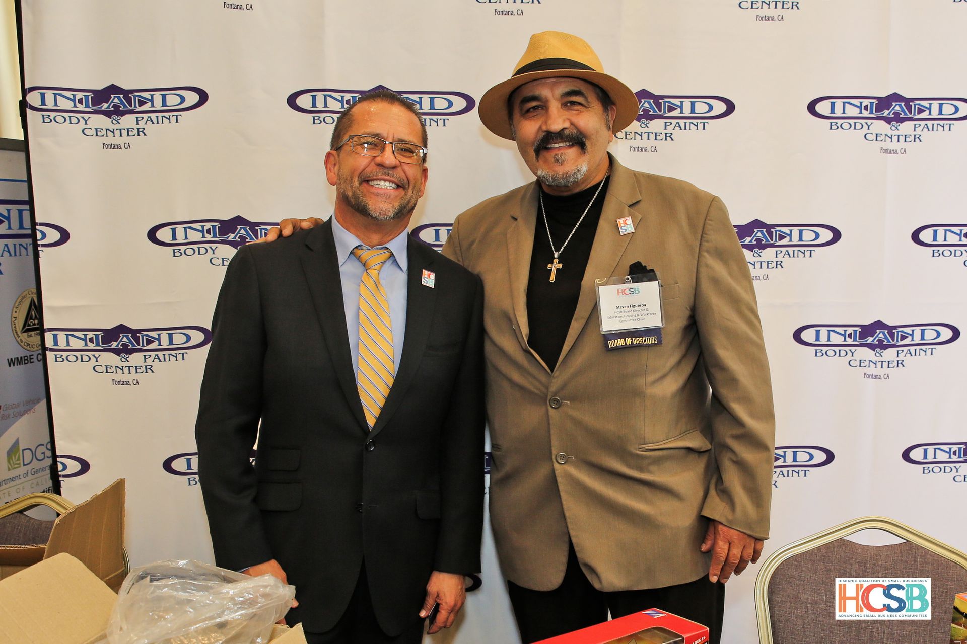 Two men are posing for a picture in front of a wall that says hcsb