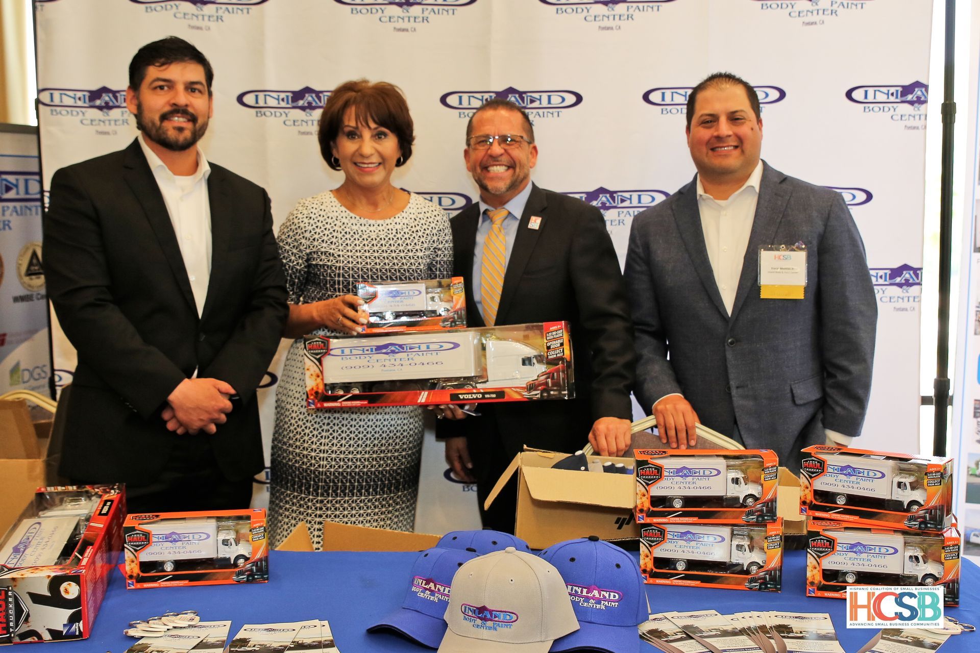 A group of people are standing around a table with boxes of toy trucks on it.