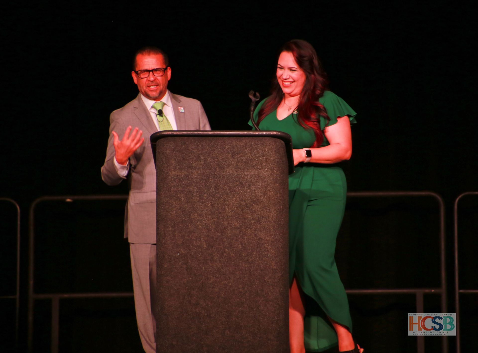 A man in a suit and tie is standing next to a woman in a green dress behind a podium.
