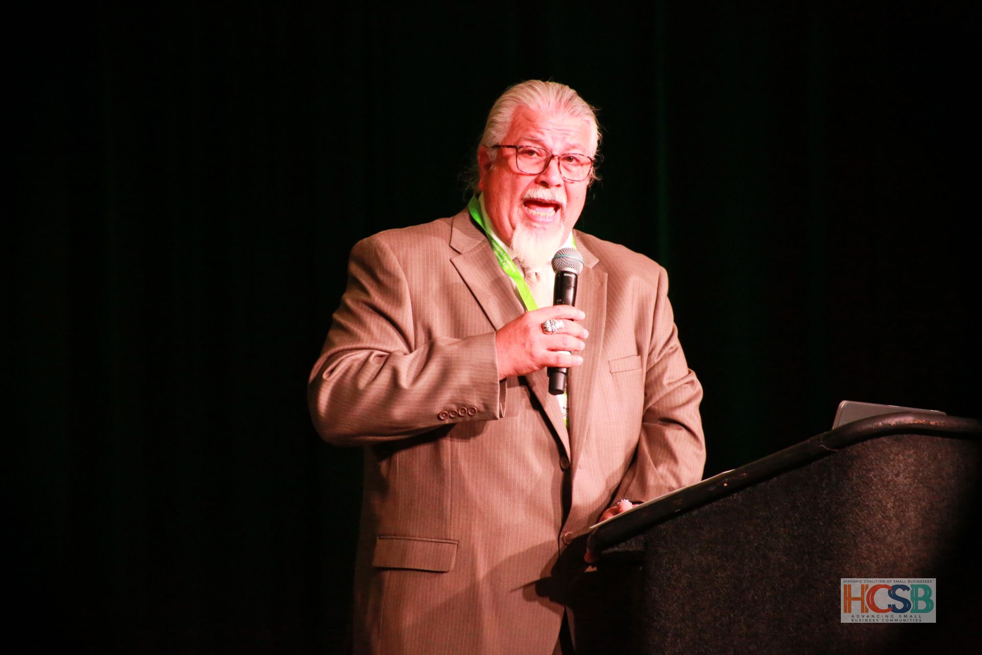 A man in a suit is standing at a podium holding a microphone.