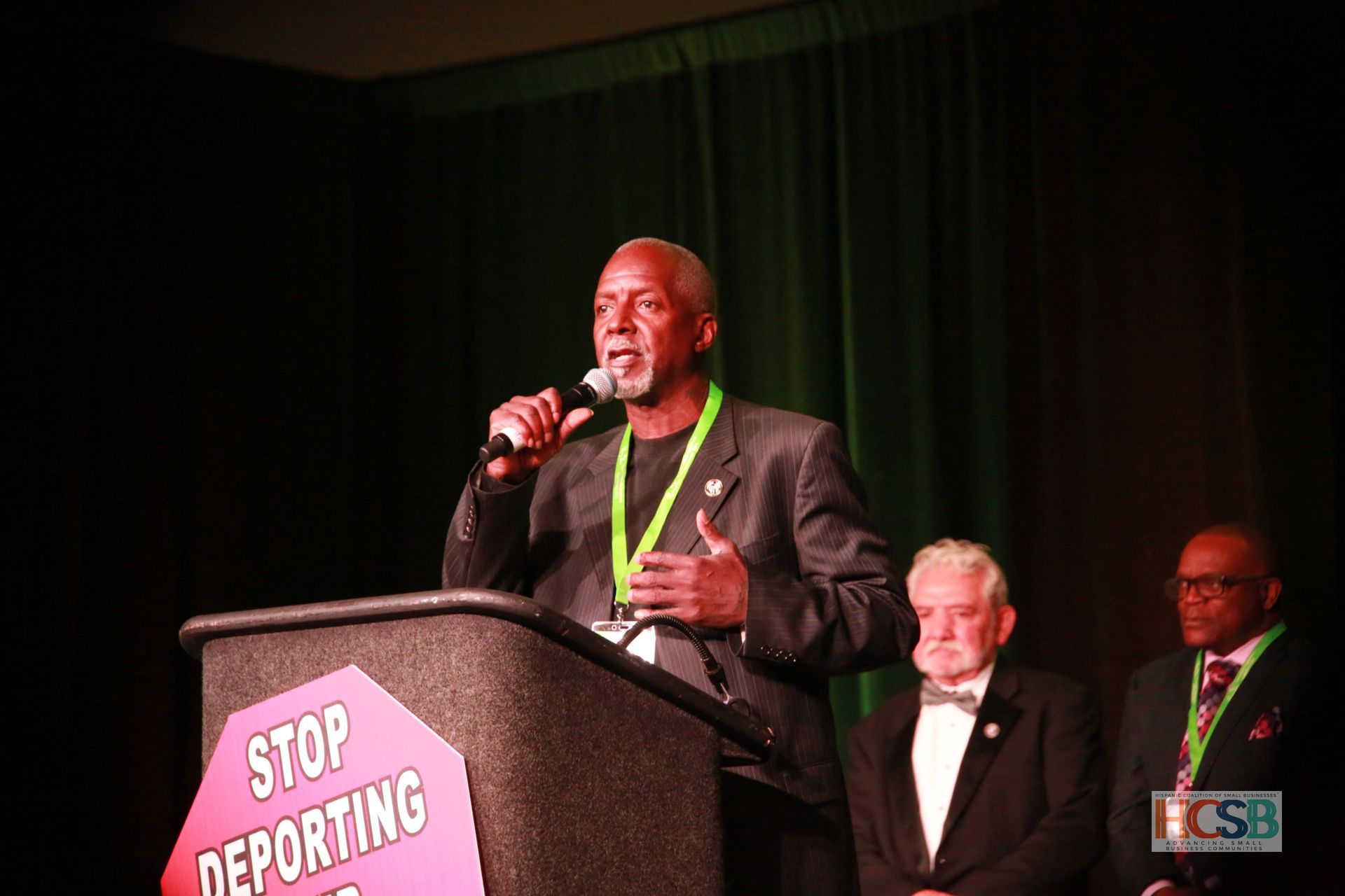 A man stands at a podium with a sign that says stop deporting
