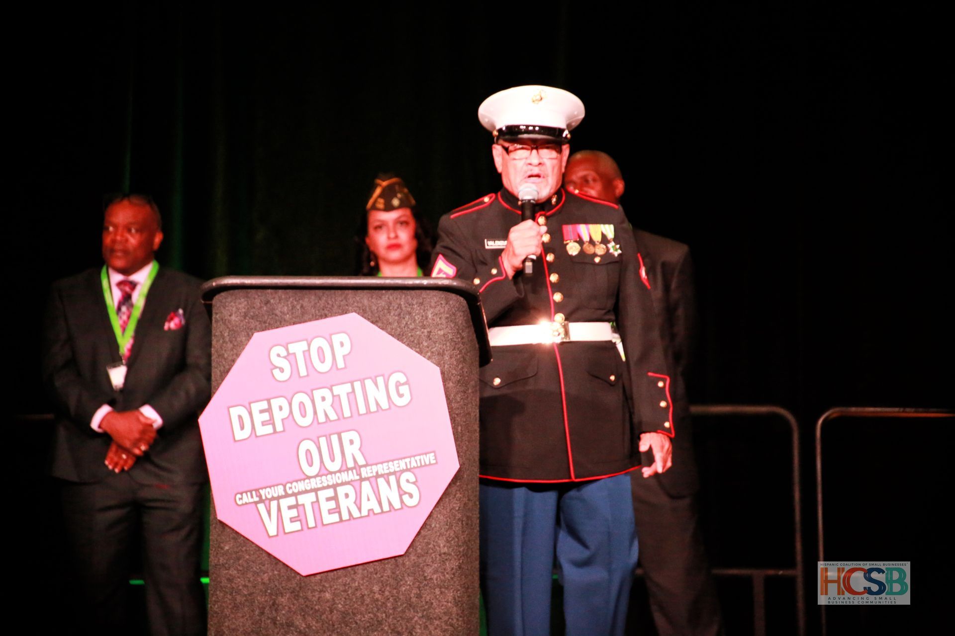 A man in a marine uniform stands behind a podium that says stop deporting our veterans
