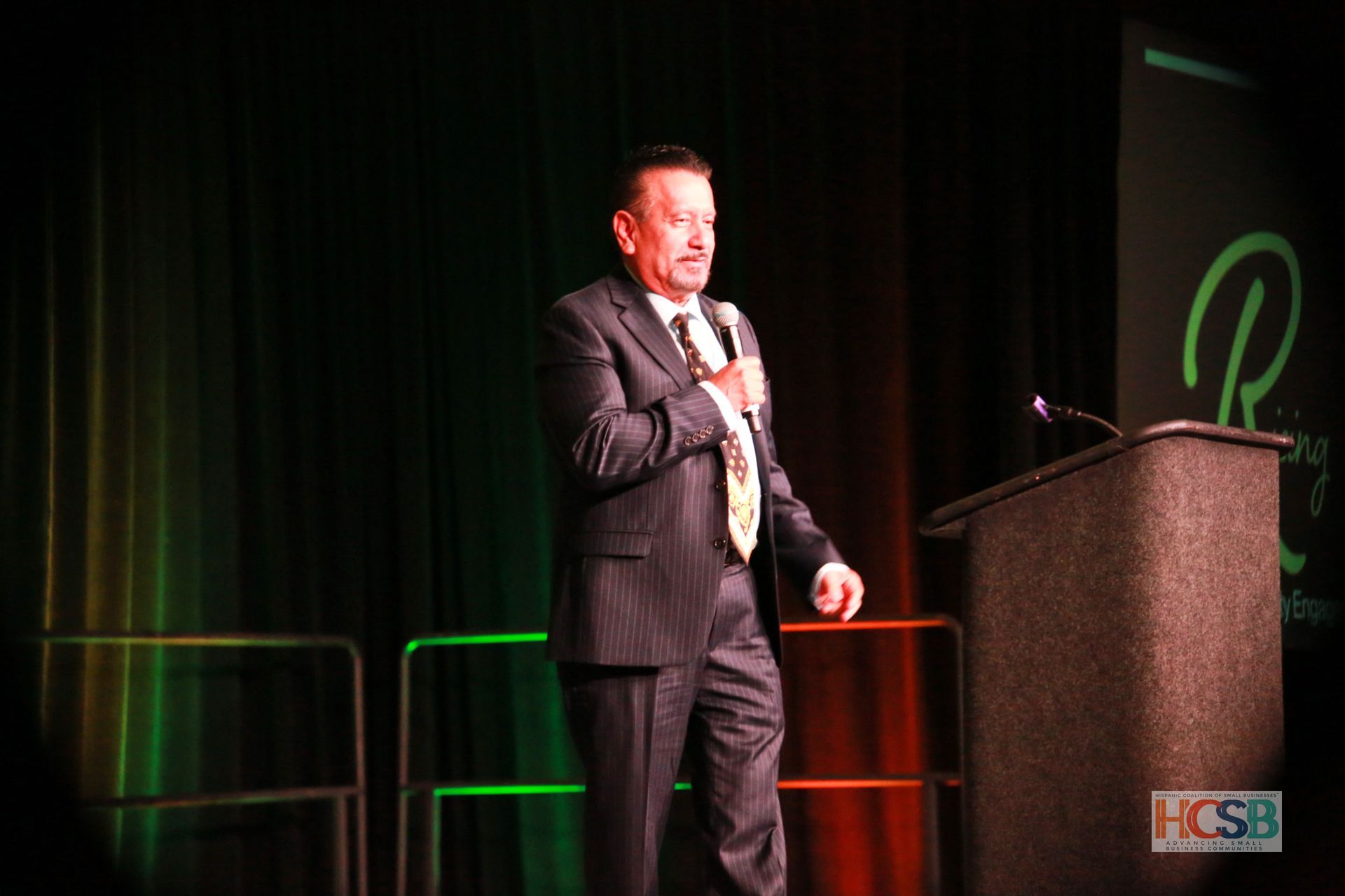 A man in a suit and tie is standing in front of a podium holding a microphone.
