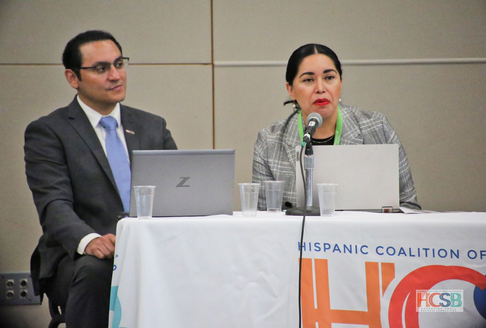 A man and a woman are sitting at a table with laptops and microphones.