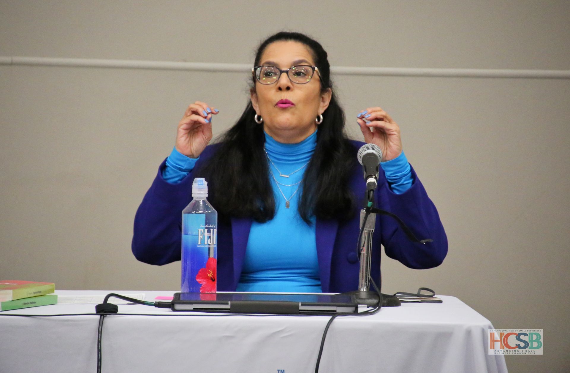A woman is sitting at a table with a microphone and a bottle of hand sanitizer