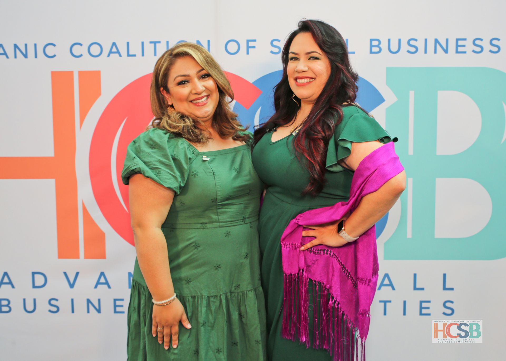 Two women are posing for a picture in front of a coalition of small business banner.
