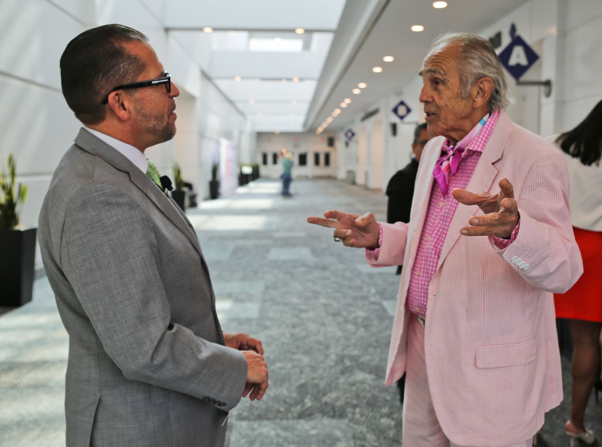 A man in a pink suit is talking to another man in a grey suit