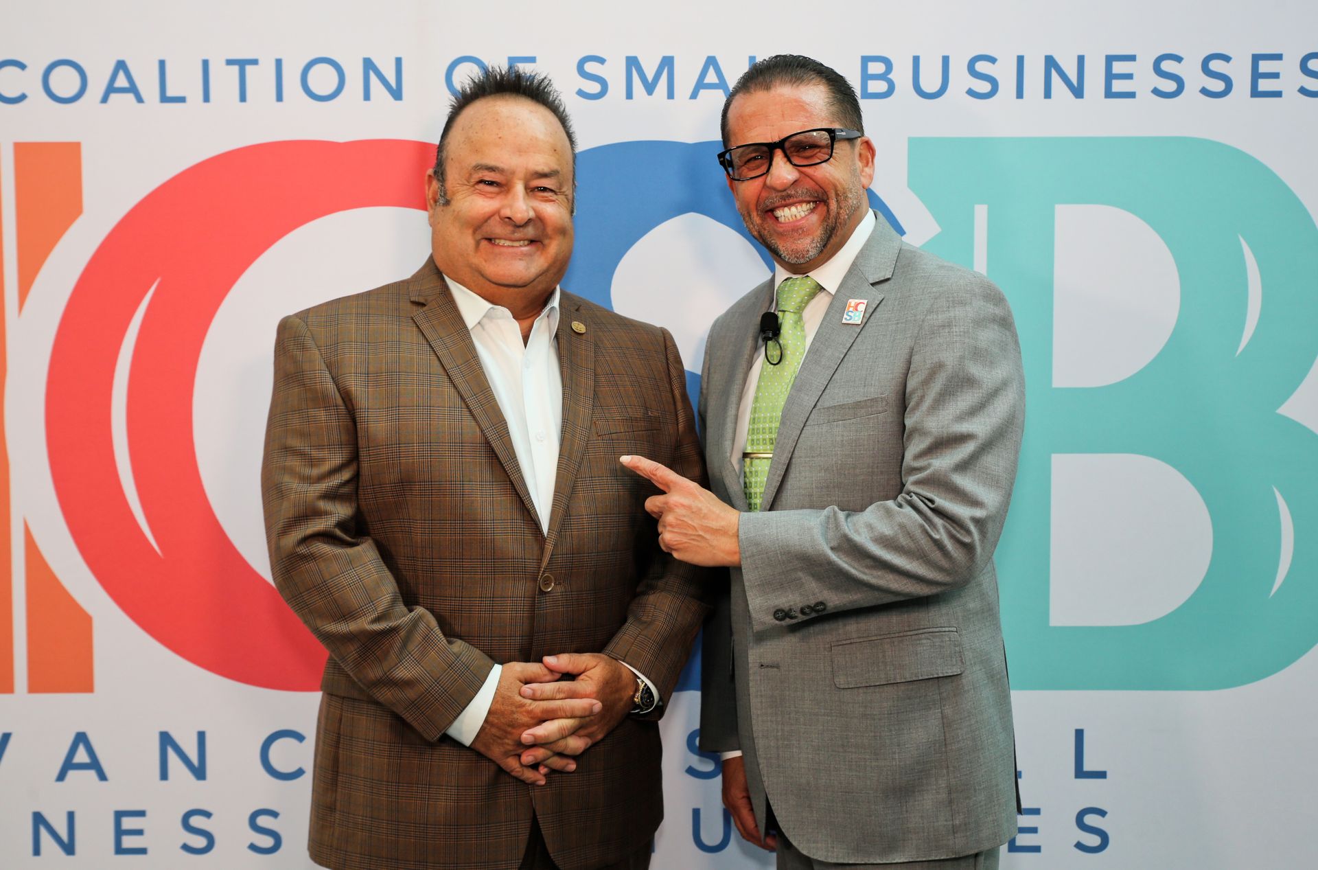 Two men are shaking hands in front of a coalition of small businesses sign