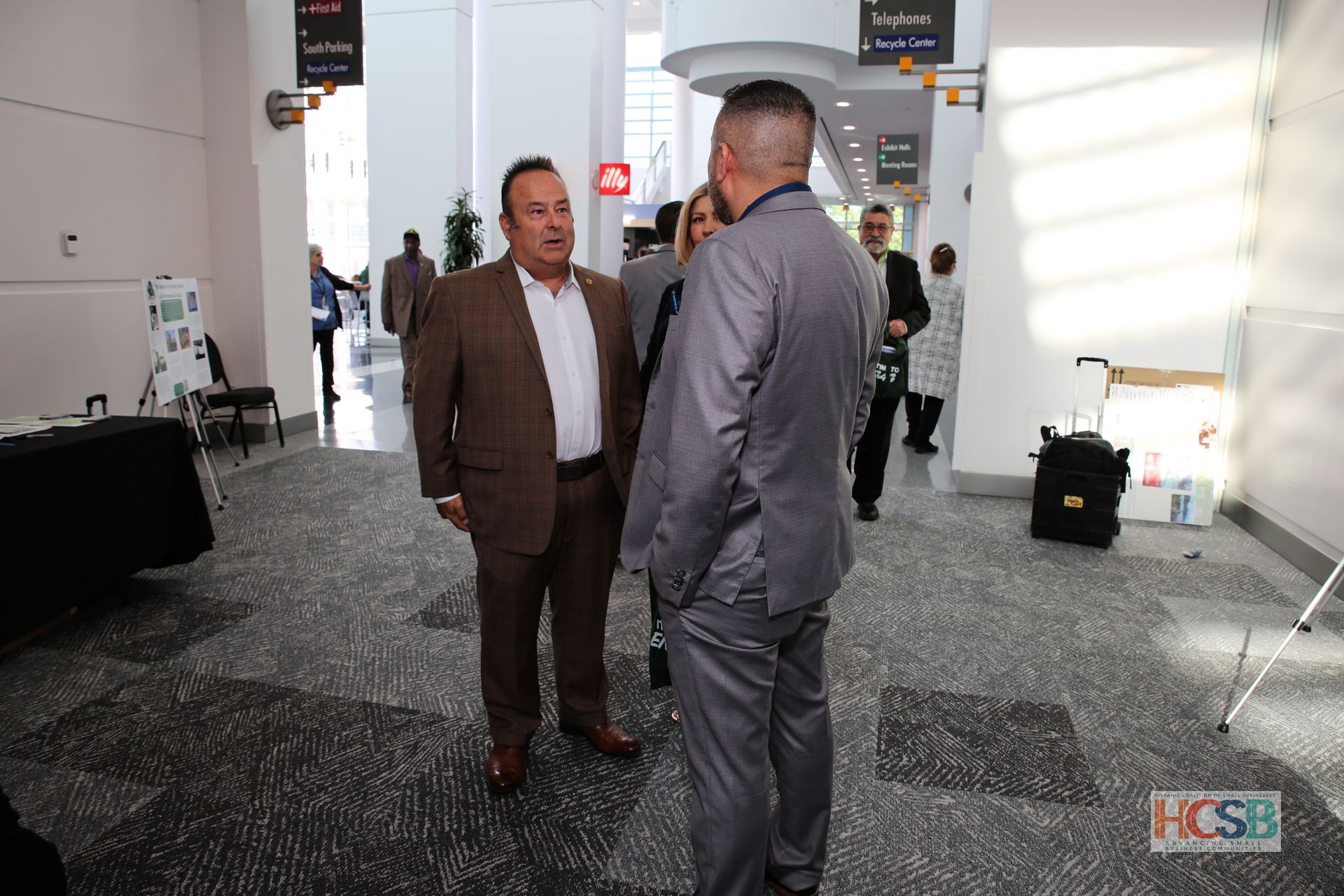 A group of men in suits are standing in a hallway and talking to each other