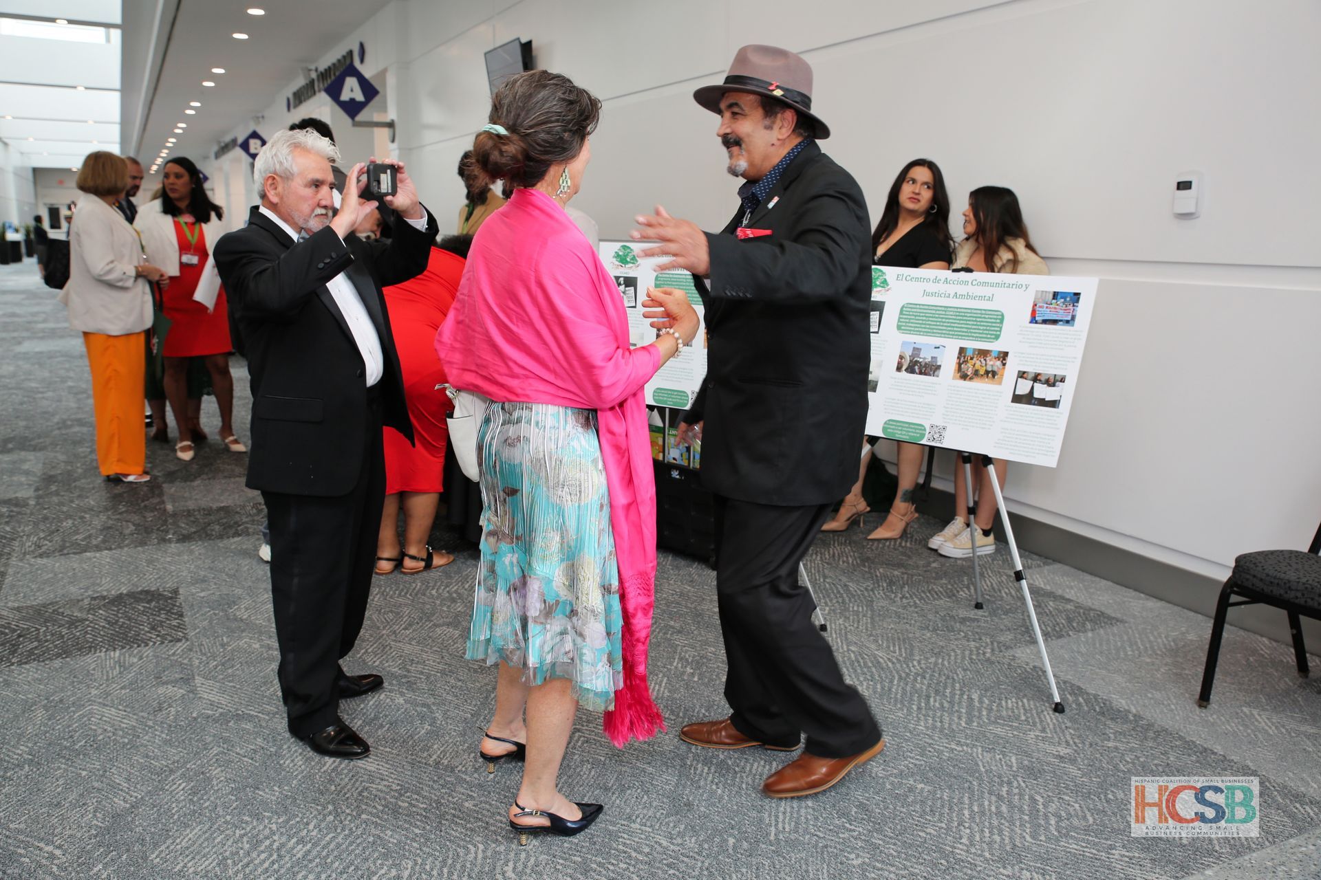 A man is taking a picture of two people dancing in front of a sign that says hcsb