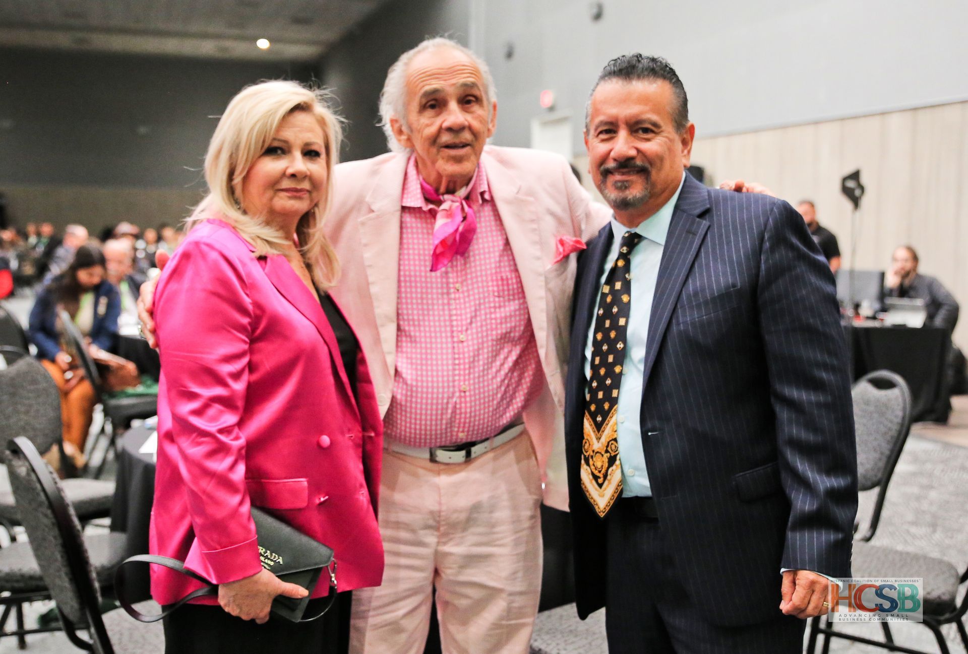 A woman in a pink jacket is posing for a picture with two men in suits.