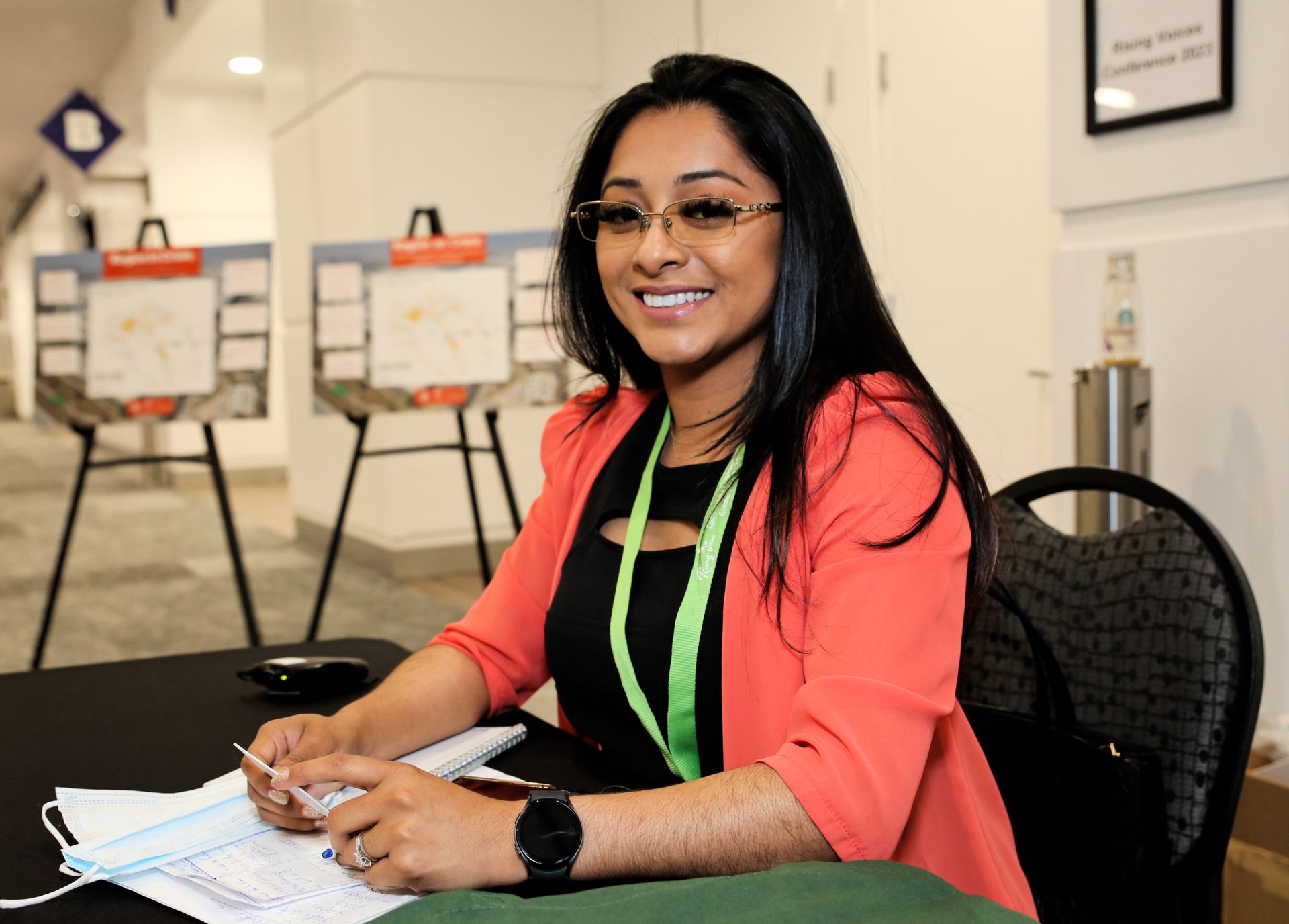 A woman is smiling while sitting at a table with papers on it.