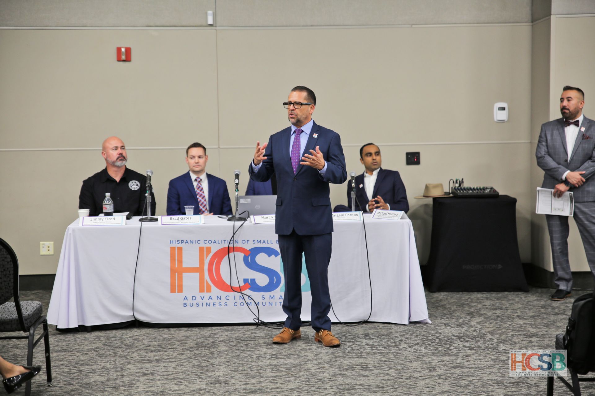 A man in a suit and tie is standing in front of a table giving a speech.