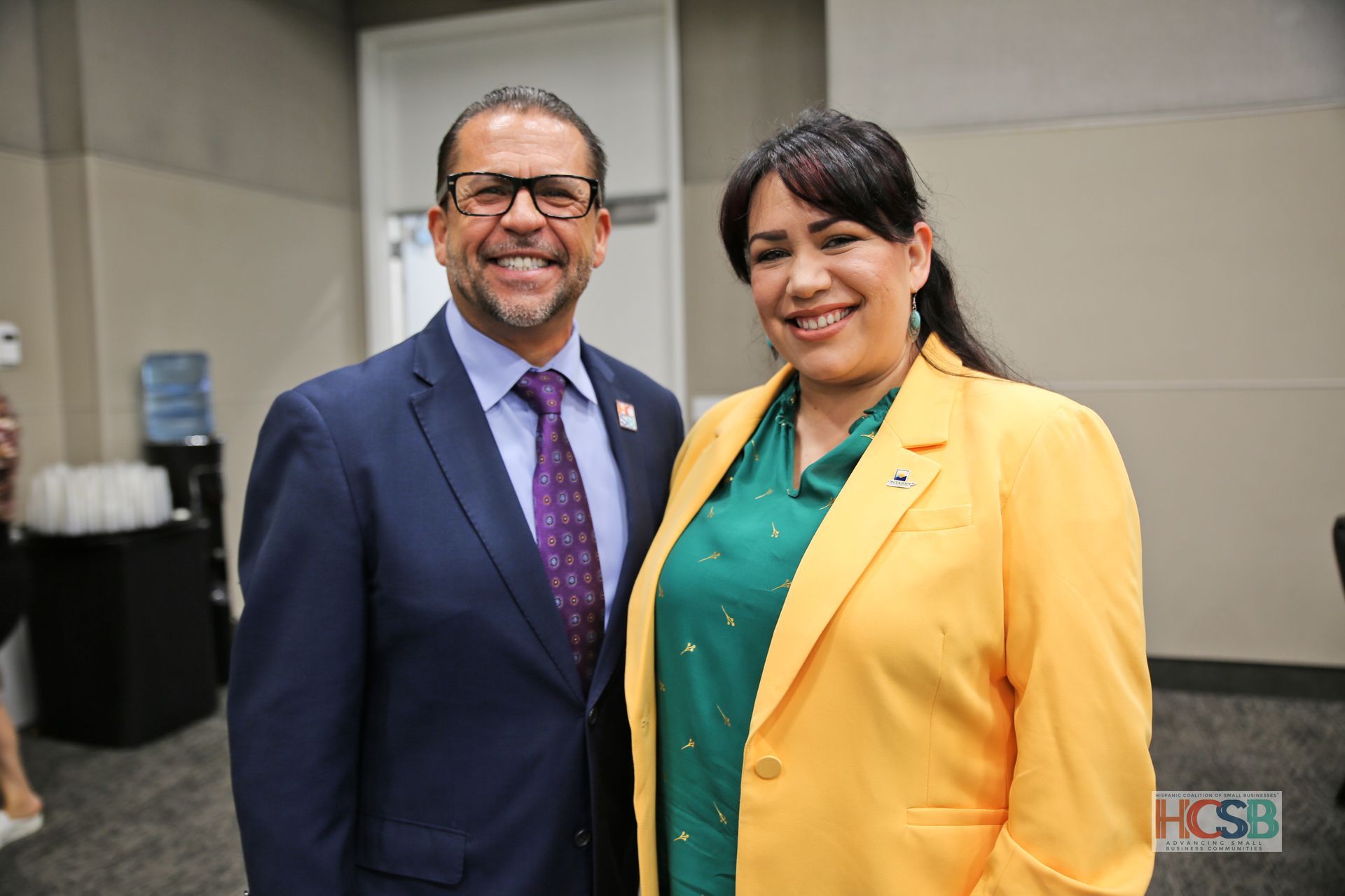 A man in a suit and tie and a woman in a yellow jacket are posing for a picture.