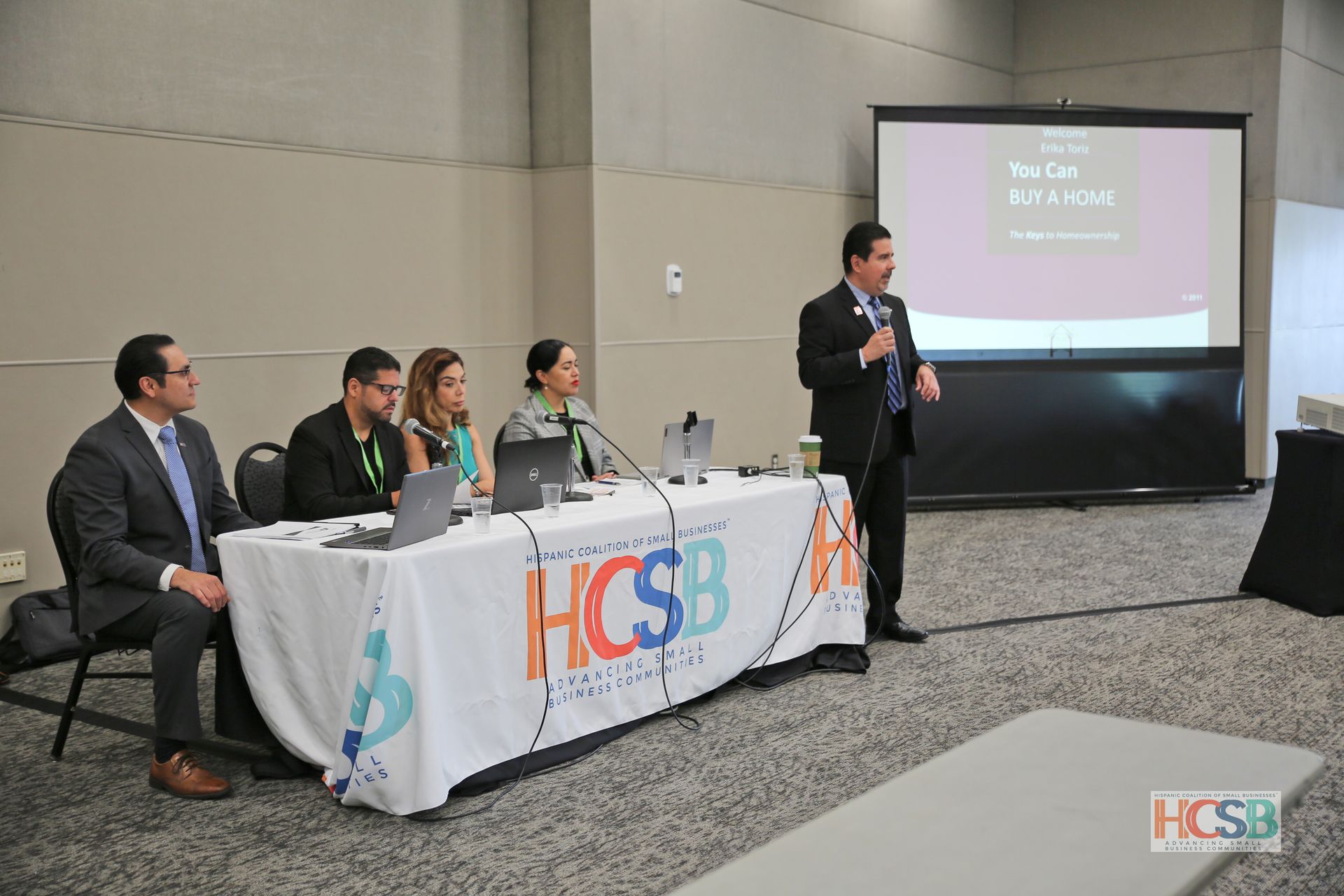 A man is giving a presentation to a group of people at a table that says hcsb on it.