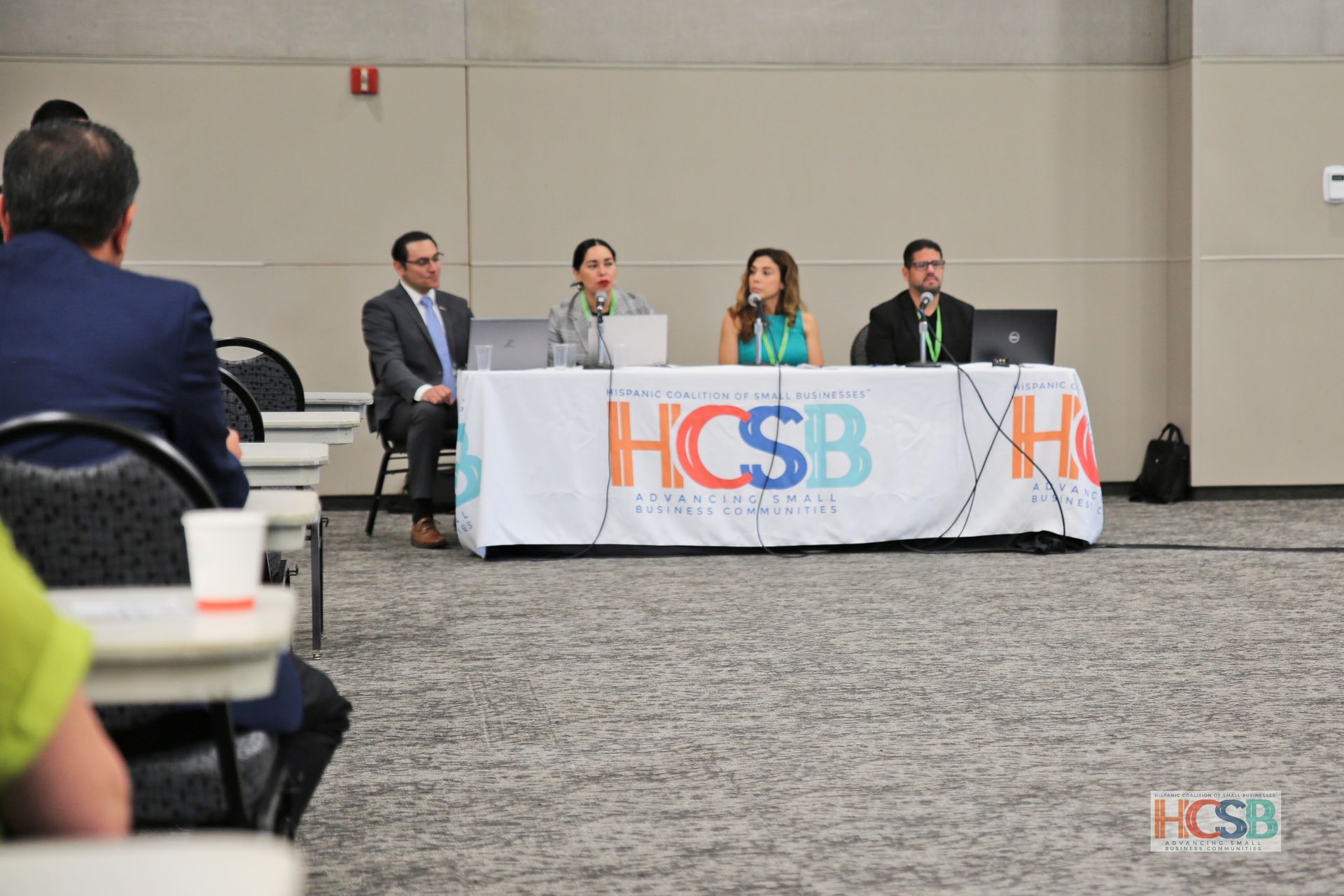 A group of people are sitting at a table with a sign that says hcsb on it.