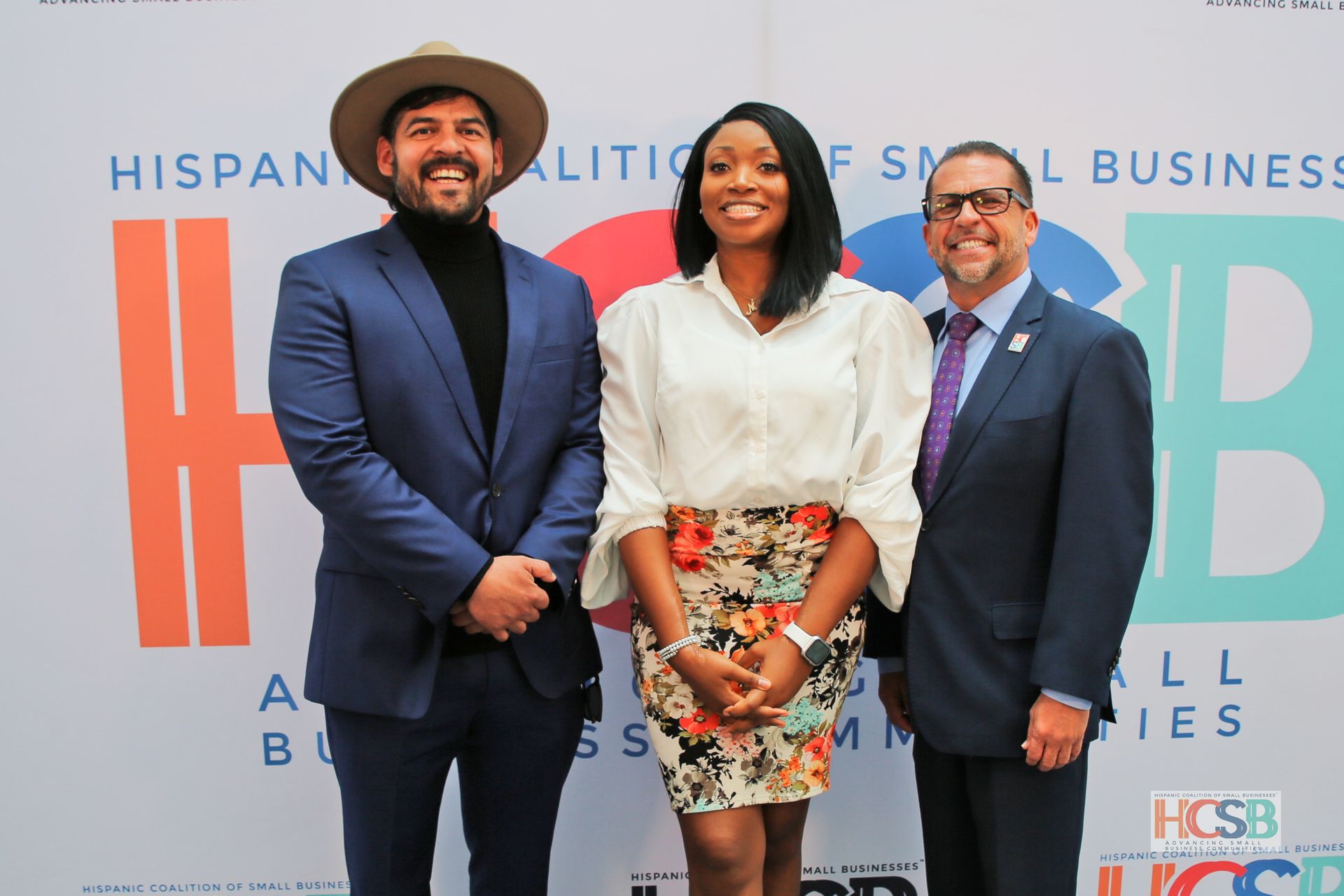 Three people are posing for a picture in front of a sign that says hispanic