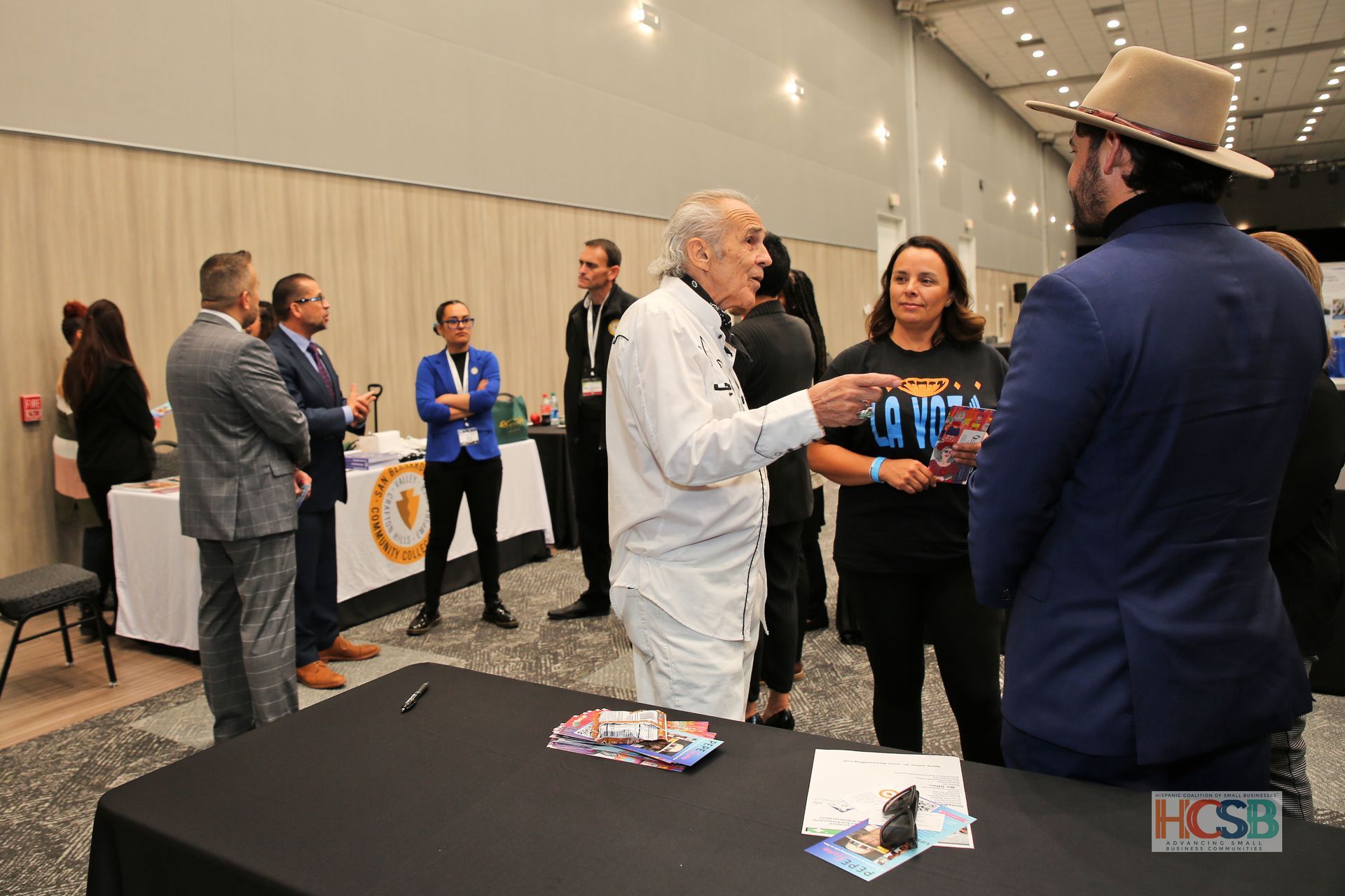 A group of people are standing around a table talking to each other.