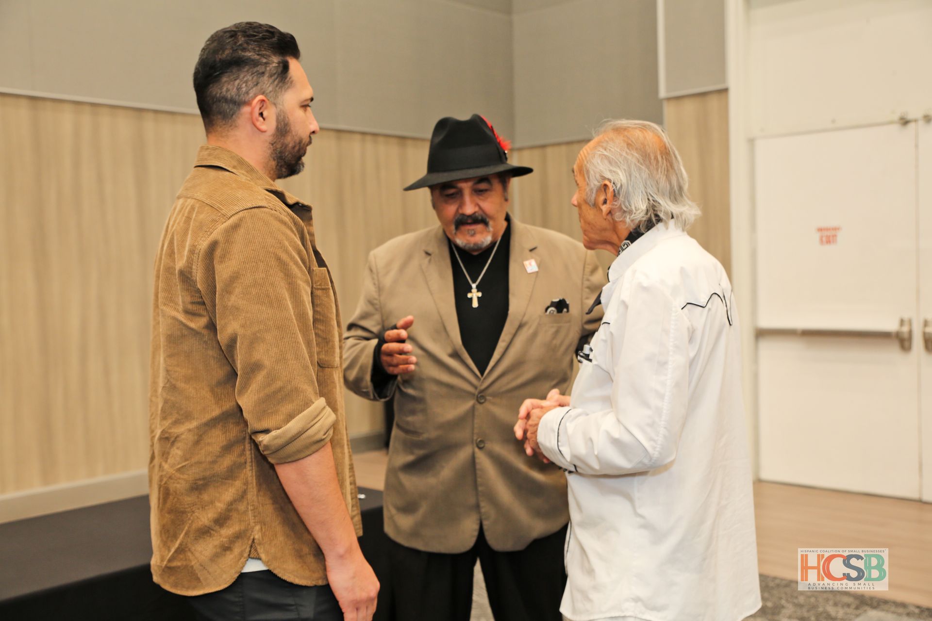 Three men are standing next to each other in a room talking to each other.