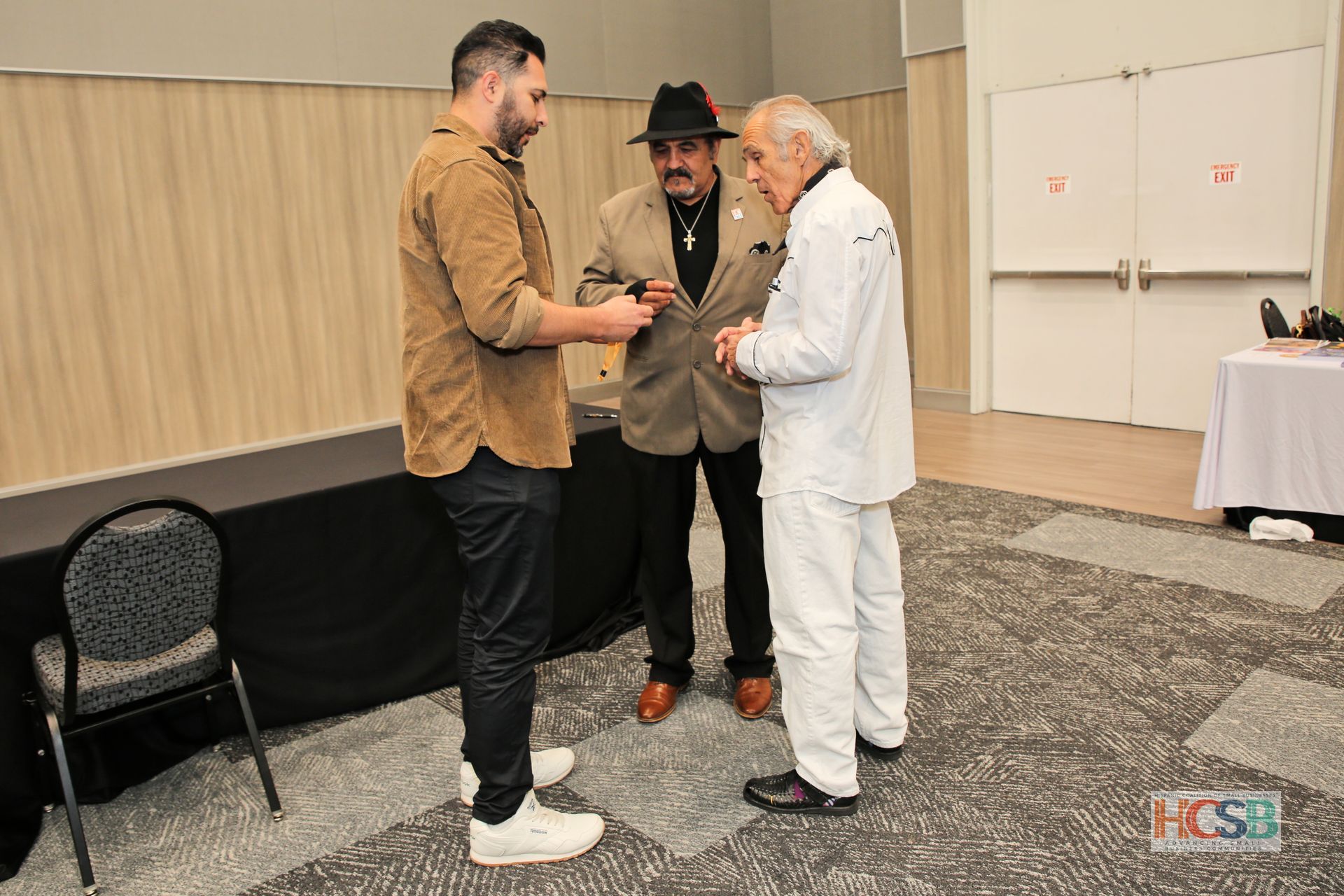 Three men are standing in a room talking to each other.