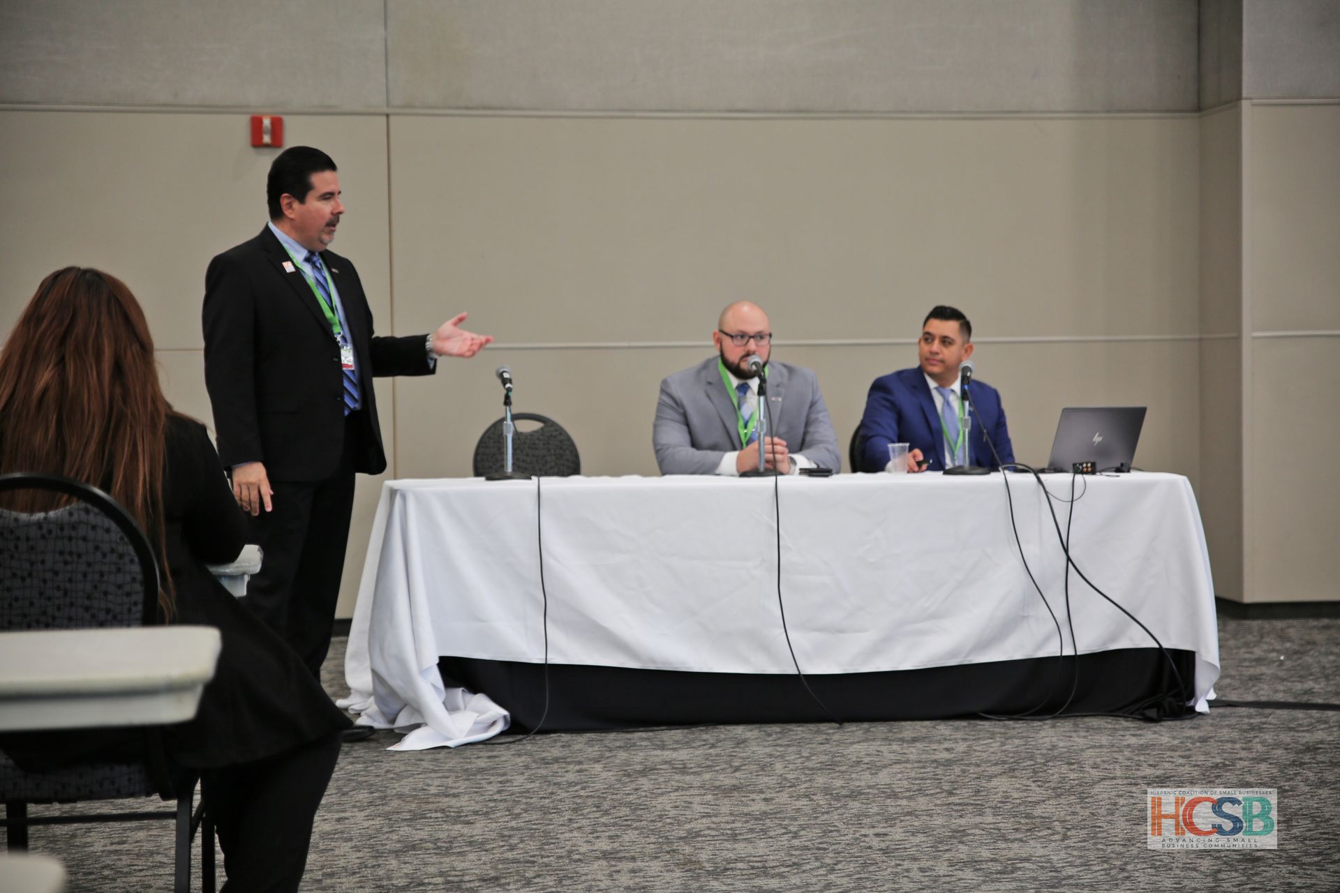 A man in a suit is standing in front of a group of people sitting at a table.