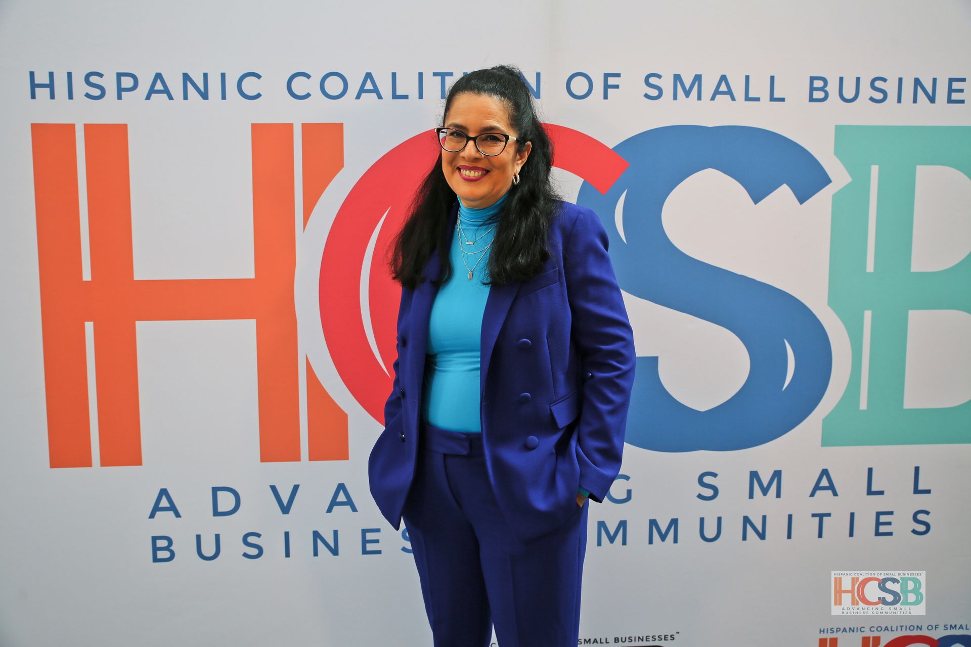 A woman in a blue suit is standing in front of a hispanic coalition of small business sign.
