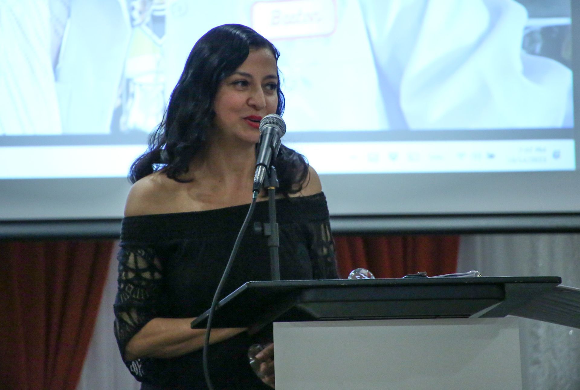 A woman is standing at a podium speaking into a microphone.