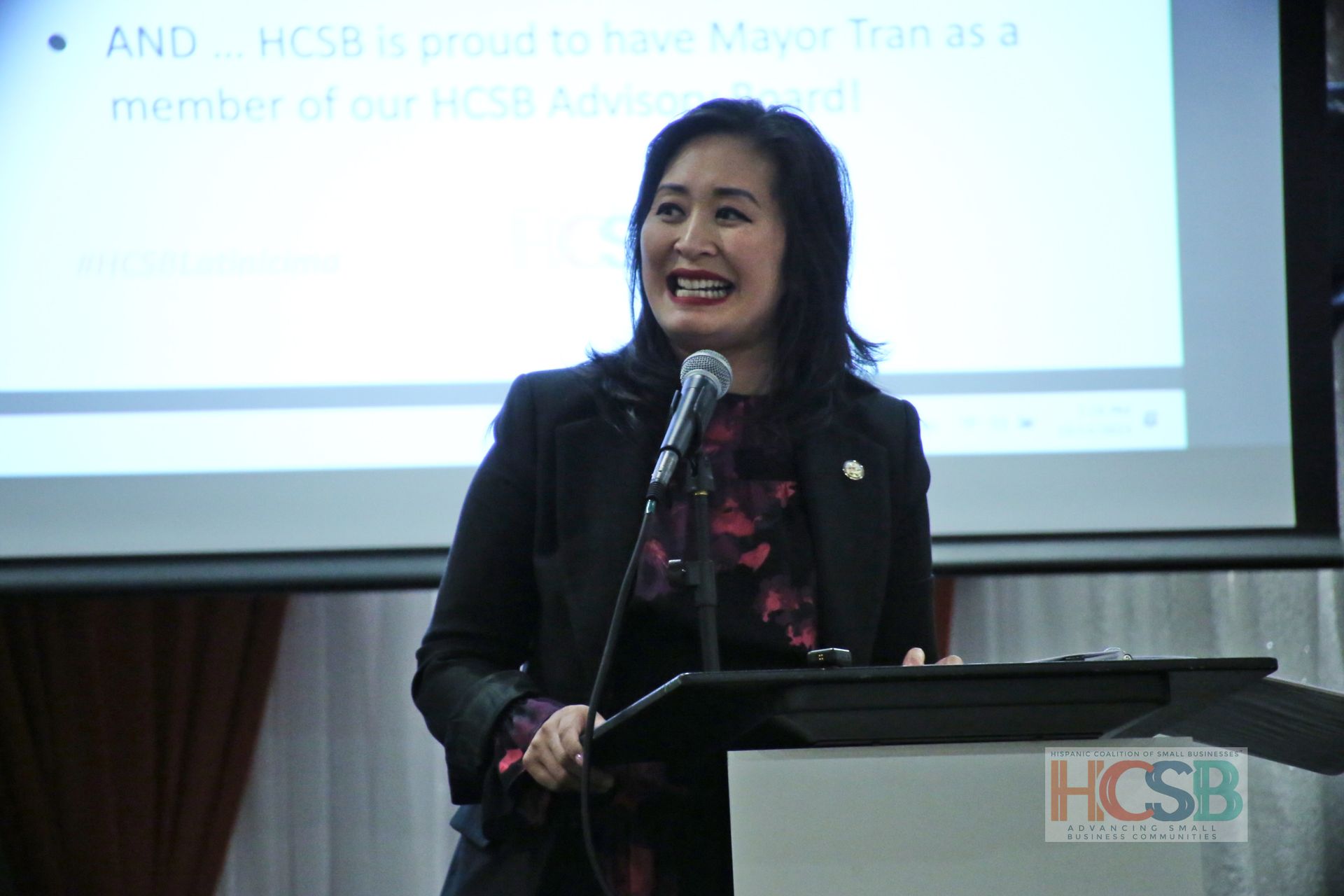 A woman is standing at a podium speaking into a microphone.