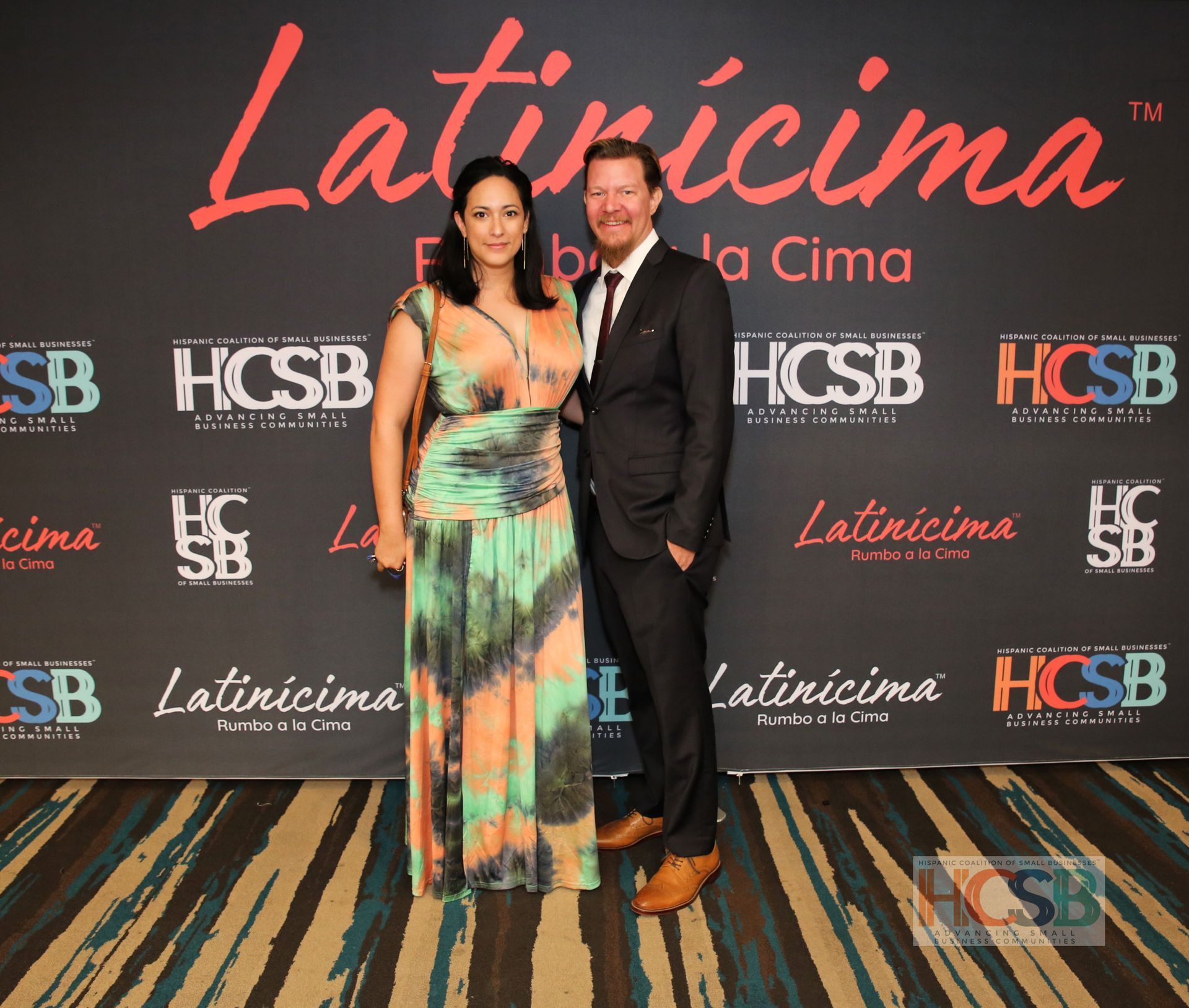 A man and woman pose in front of a wall that says latincima