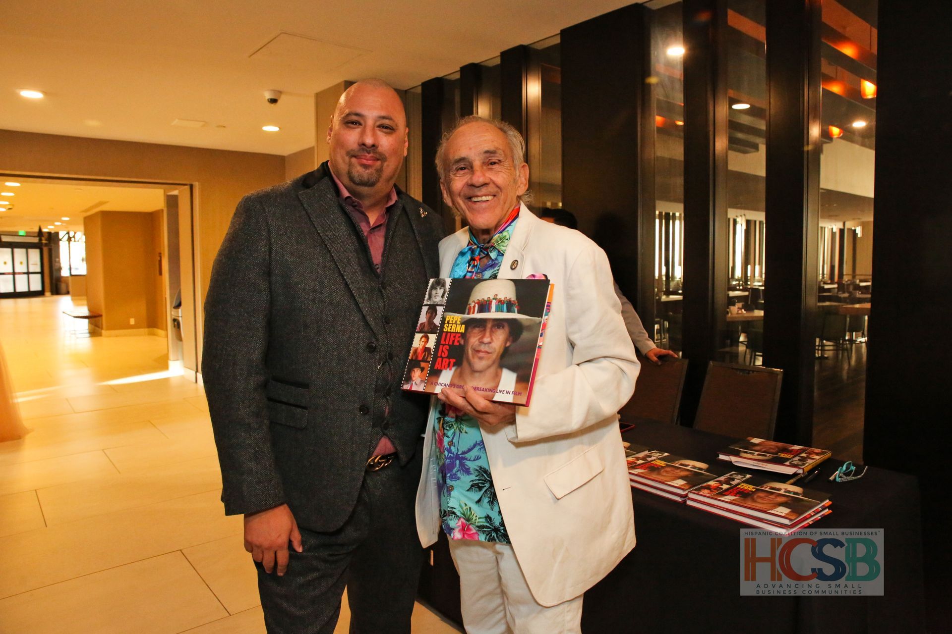 Two men are standing next to each other and one is holding a book