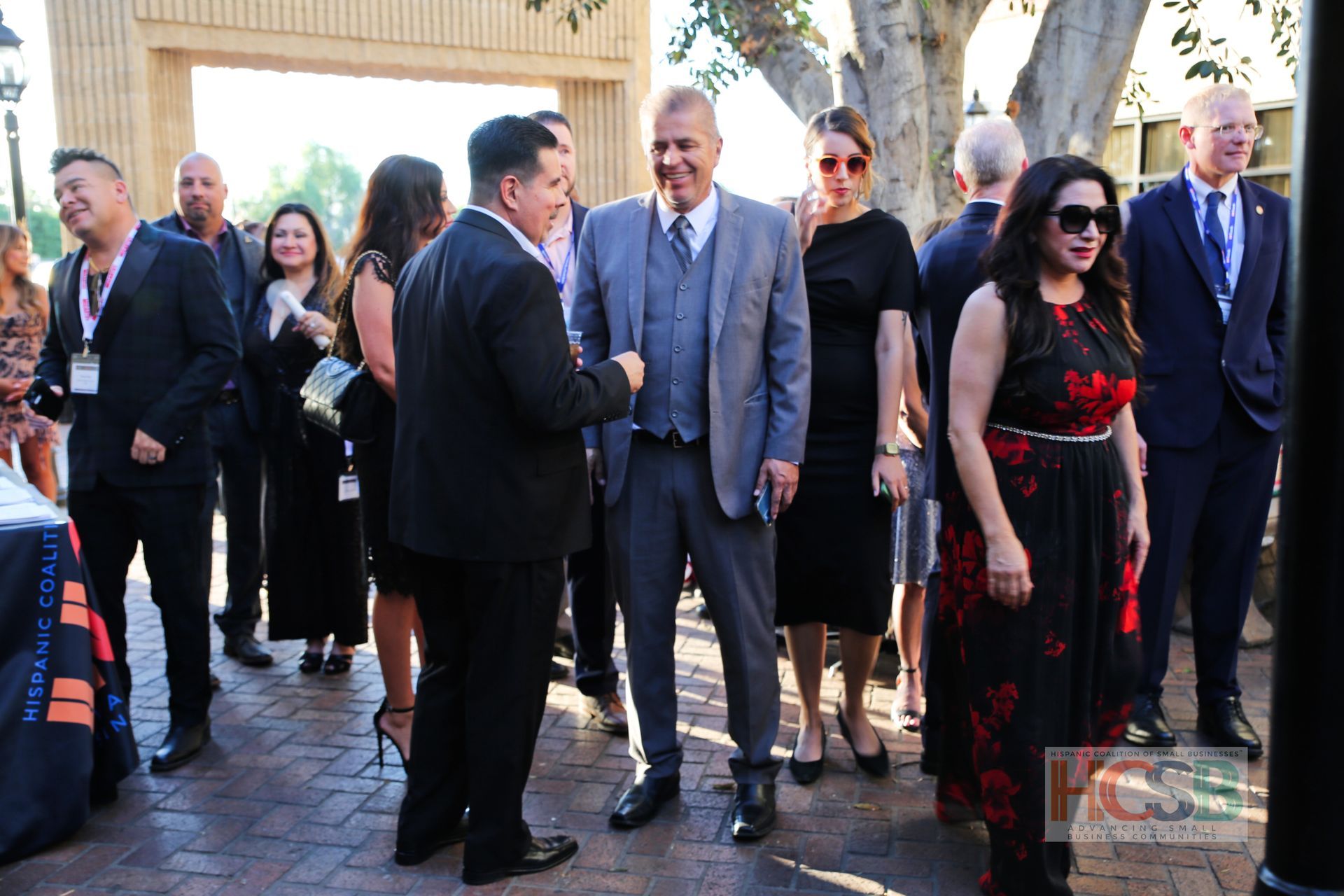 A group of people are standing on a brick sidewalk talking to each other.